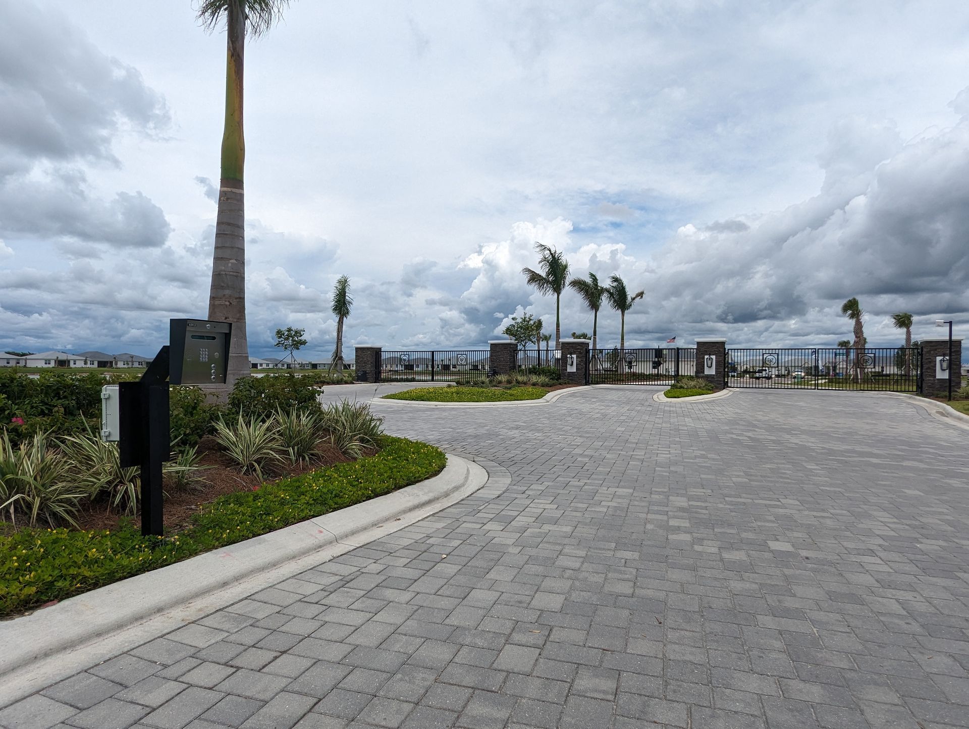 Curved stone walkway in a landscaped waterfront park with palm trees under a cloudy sky
