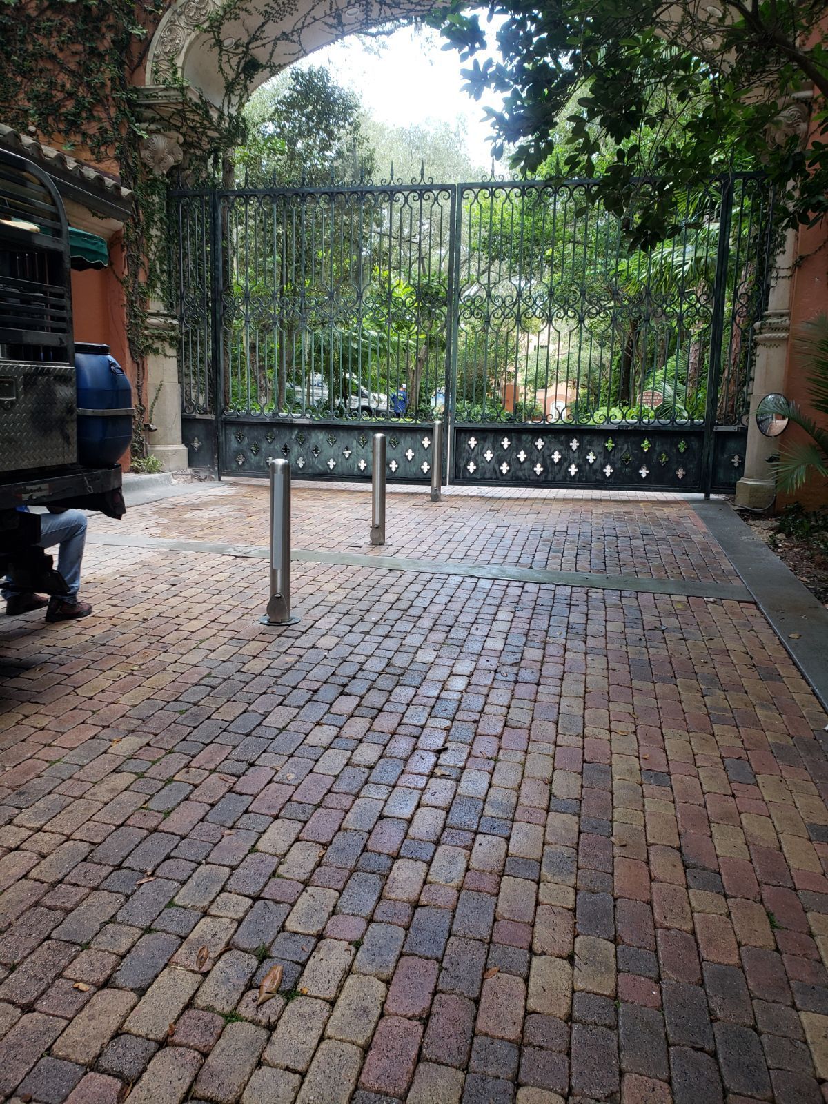 Brick-paved courtyard with a closed metal gate and garden beyond