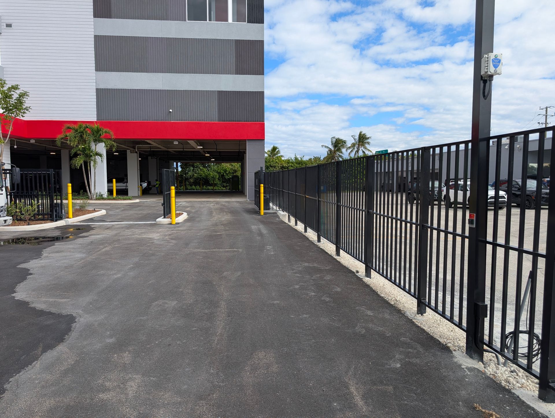 Building entrance driveway beside black fence under a cloudy blue sky