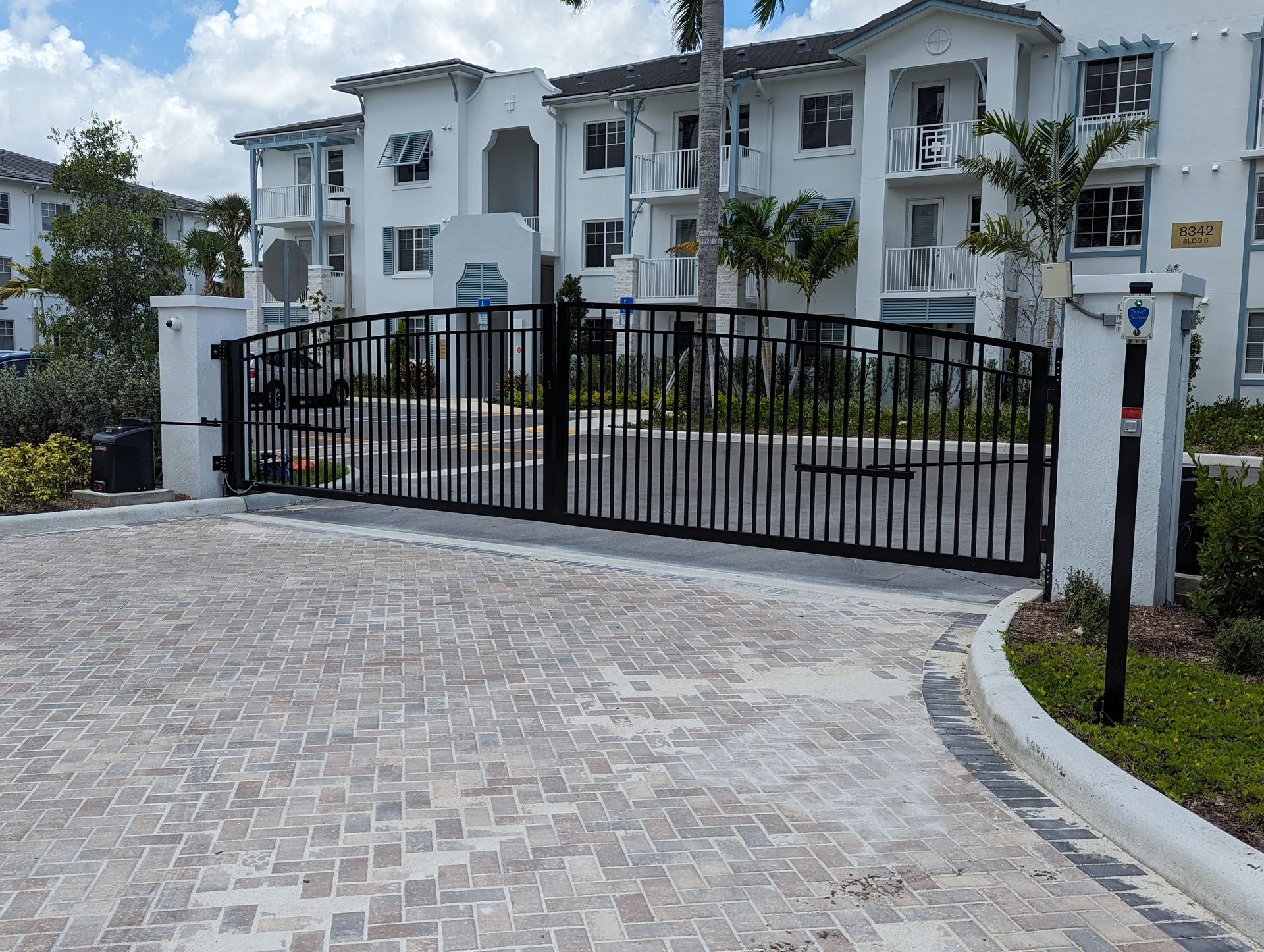 Gated entrance to a white apartment complex with a paved driveway and palm trees