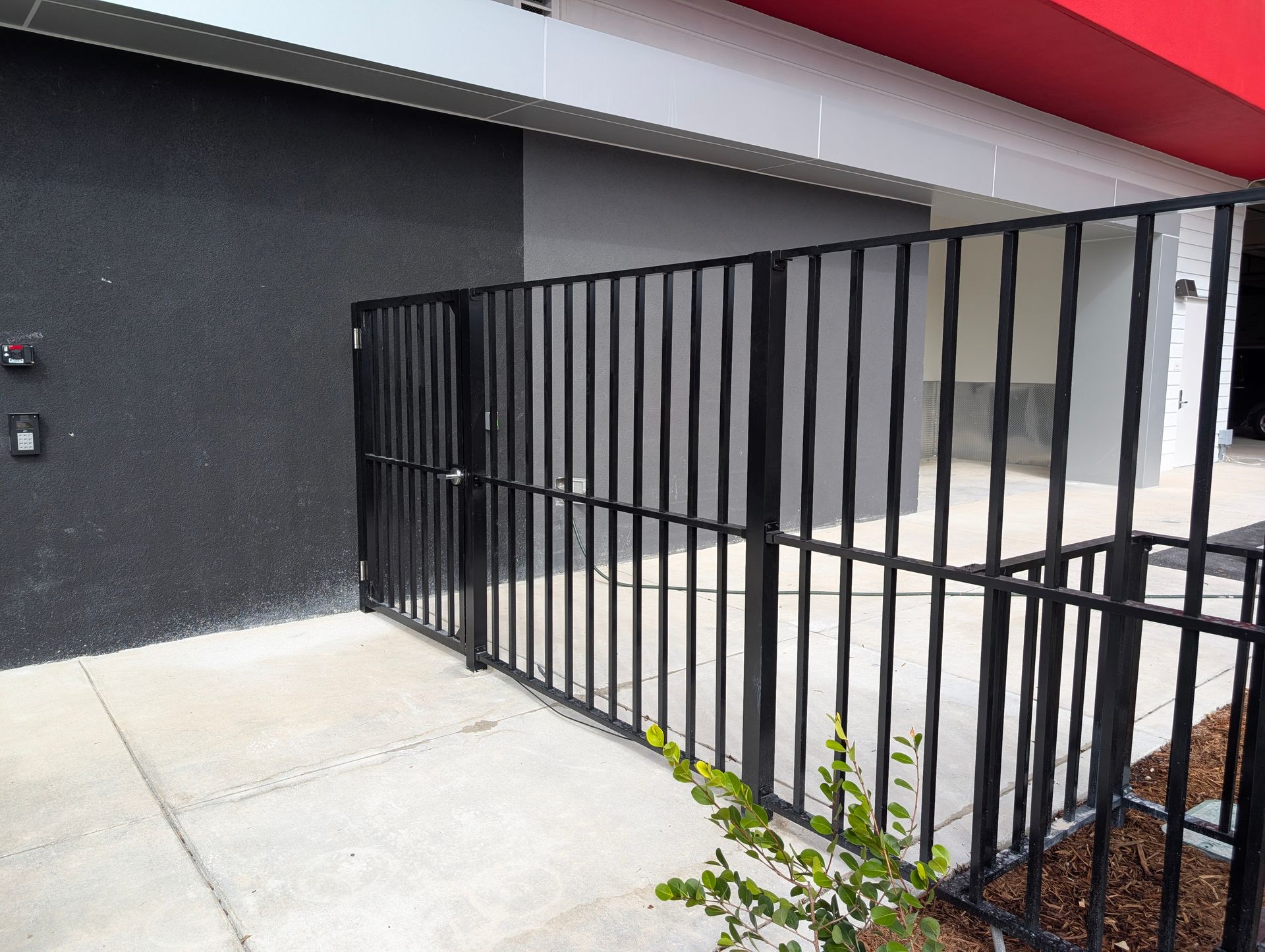Black metal security gate beside a dark exterior wall and concrete walkway under a covered entryway