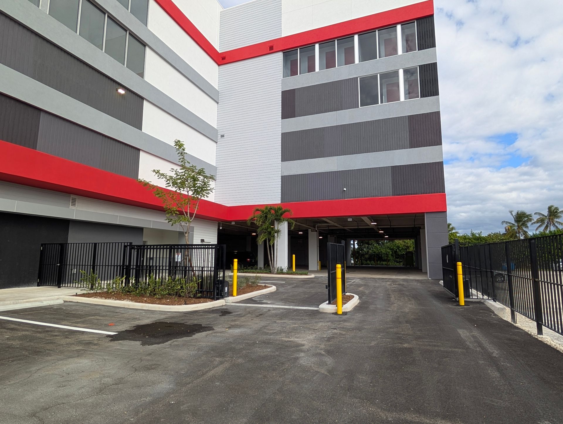 Modern apartment building entrance with red-gray facade, driveway, and yellow bollards at the gate