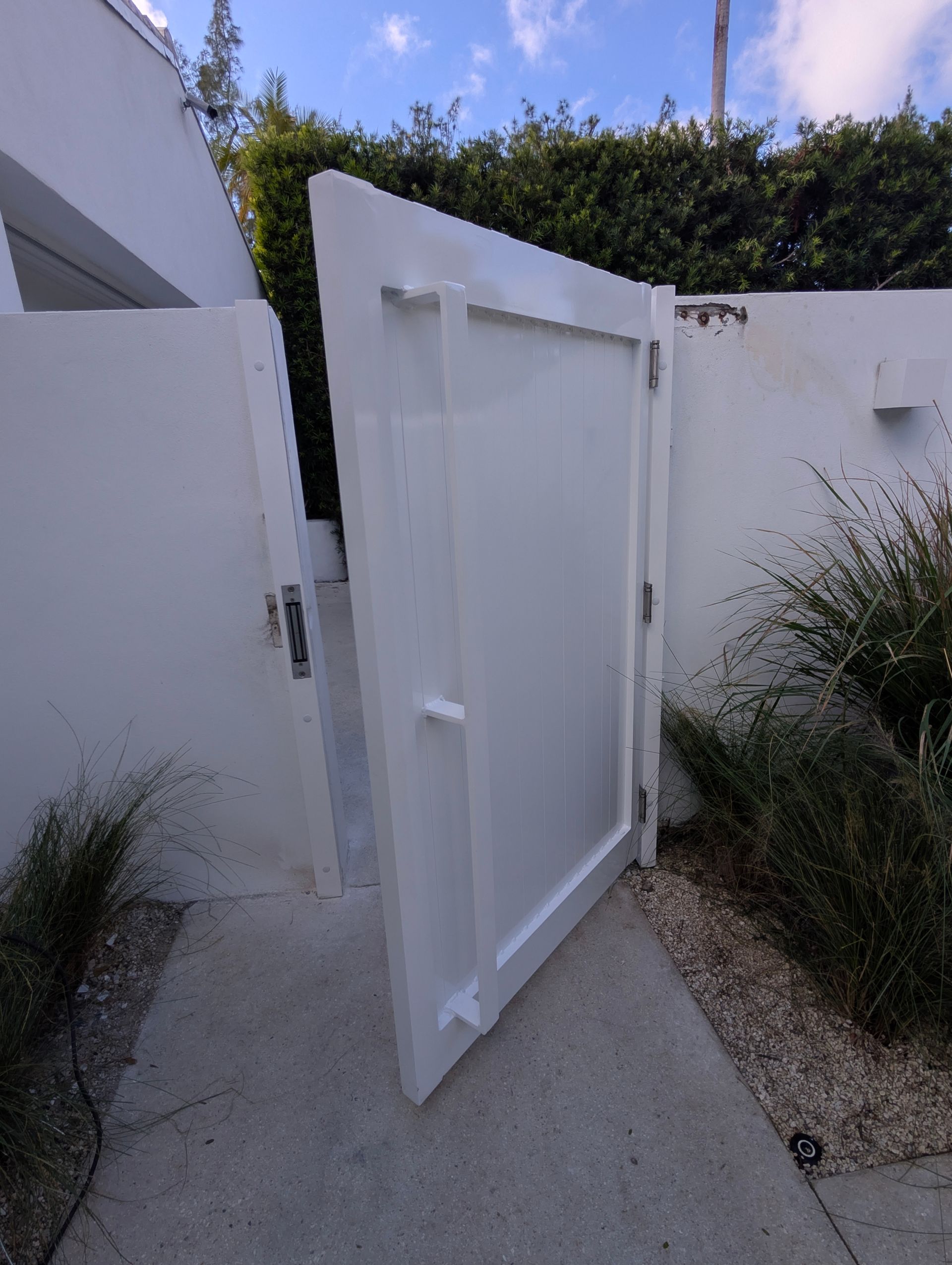 Open white gate in a concrete walkway beside white walls and desert plants at dusk
