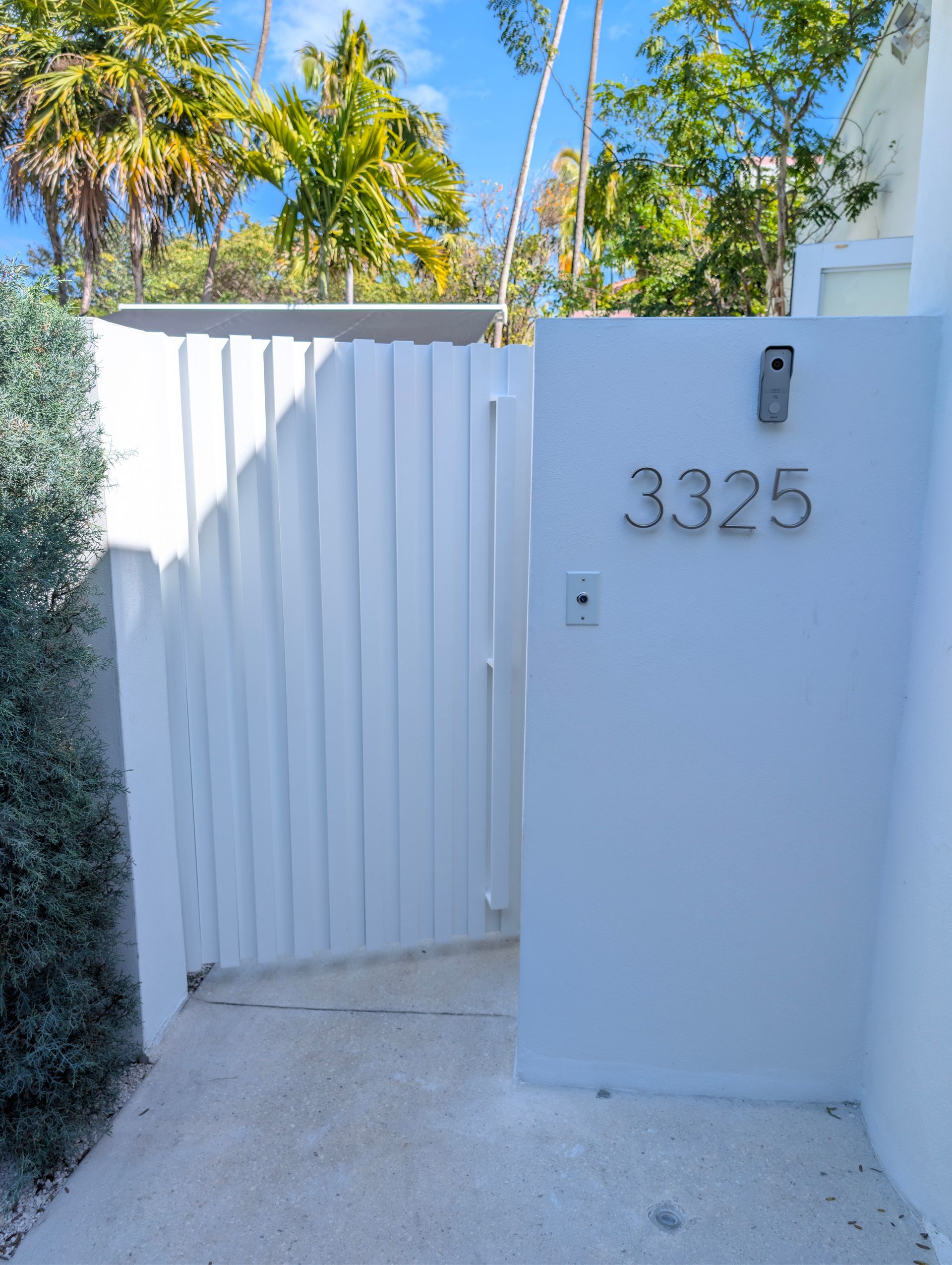 White gate and entry wall with house number 3325 in a sunny tropical courtyard
