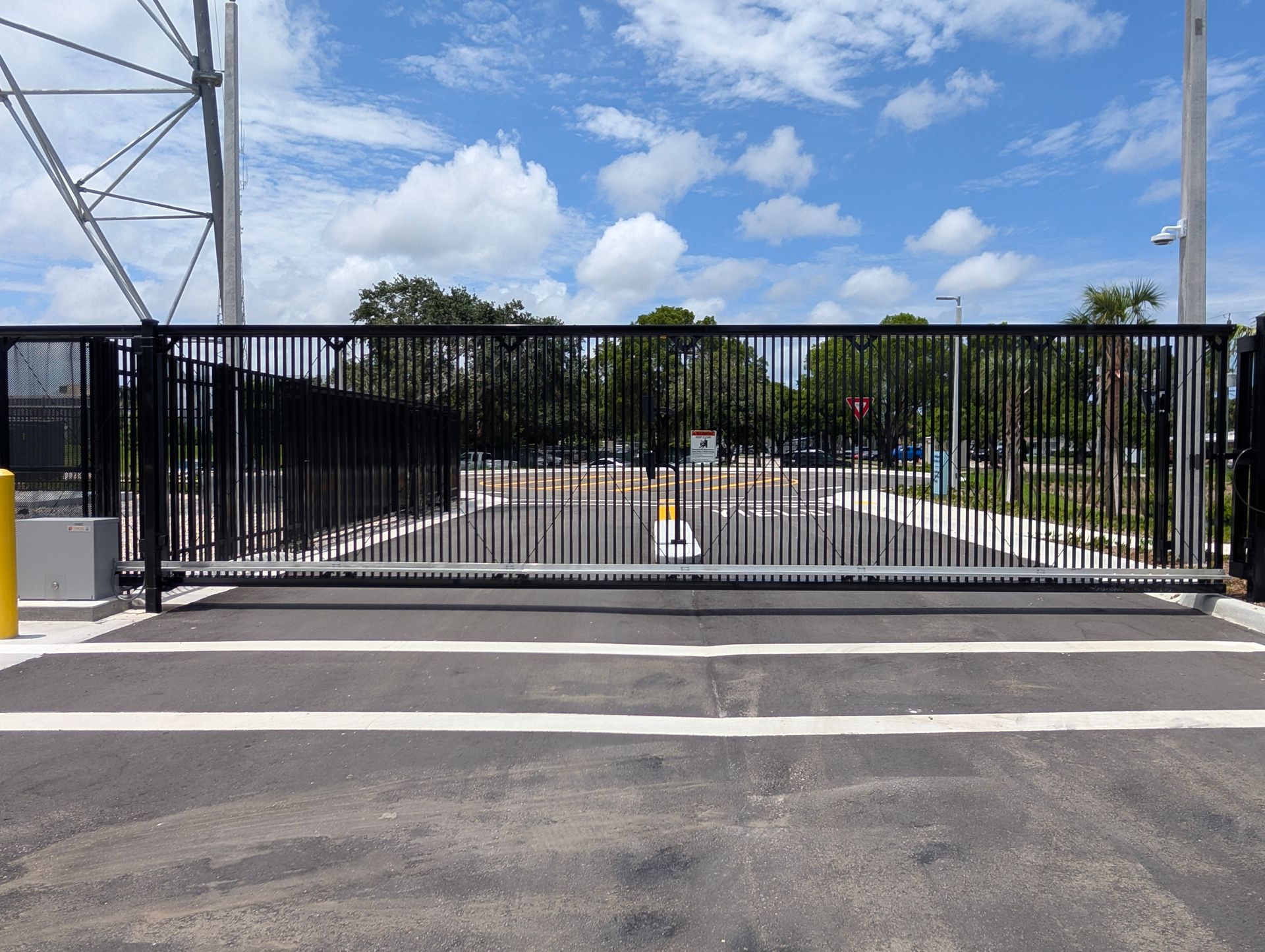 Black metal gate blocking a paved roadway, with power lines and blue sky behind it