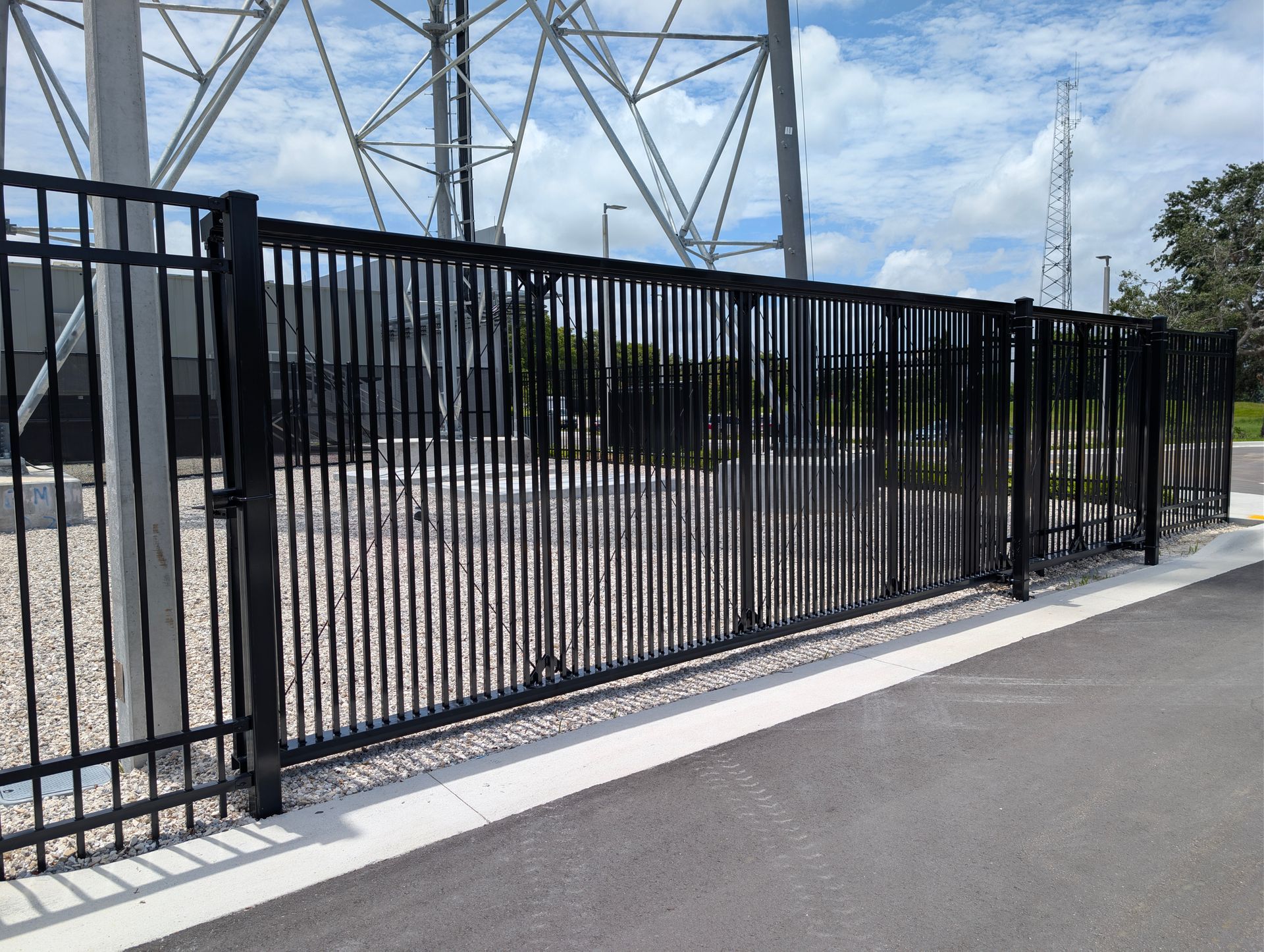 Black metal fence beside a paved road, with power lines and trees in the background.
