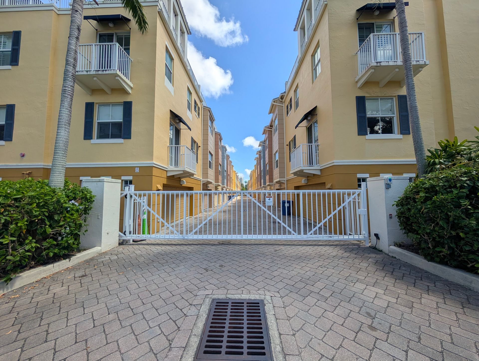 Gated entrance between beige apartment buildings under a blue sky with clouds