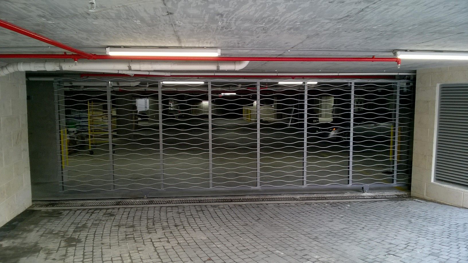 Underground garage entrance with closed metal gate, concrete ceiling, and tiled floor.