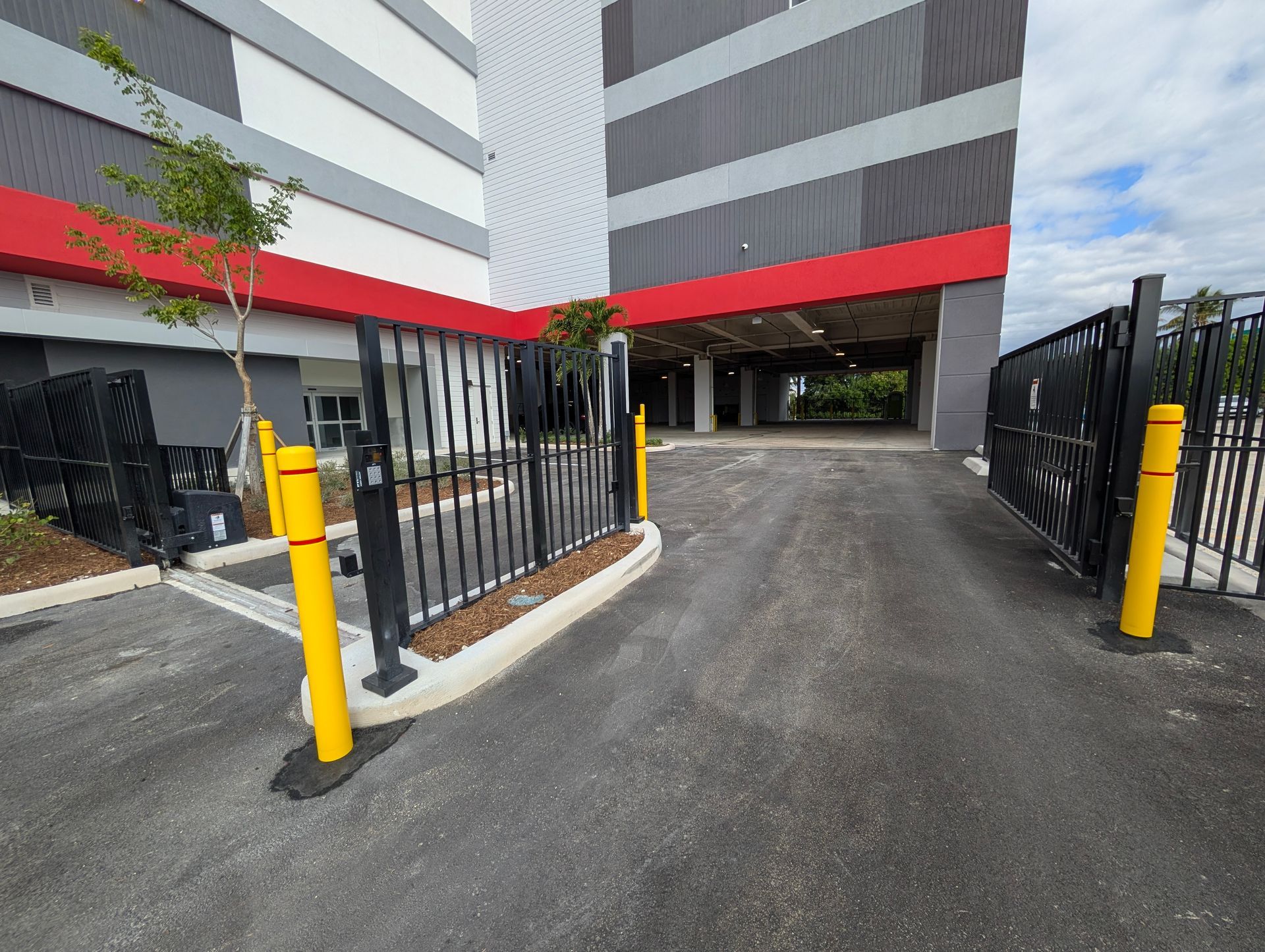 Gated driveway between modern apartment buildings with yellow bollards and black fencing
