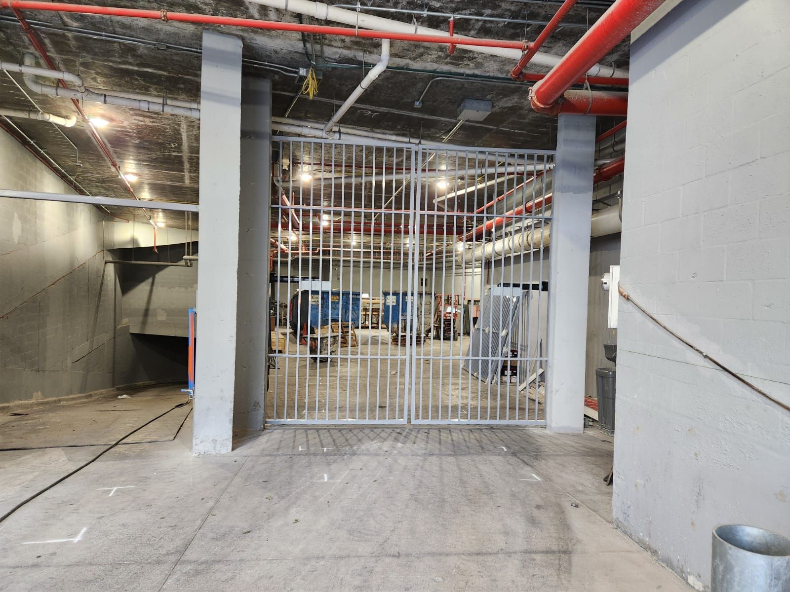 Industrial interior with red ceiling pipes and a white metal security gate blocking an open storage area