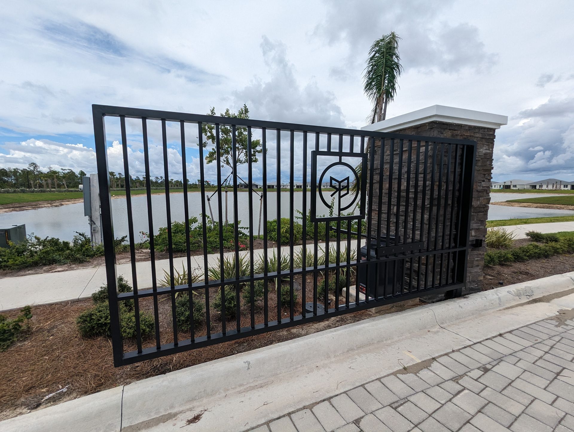 Black metal gate beside a paved path, overlooking a lake under a cloudy sky