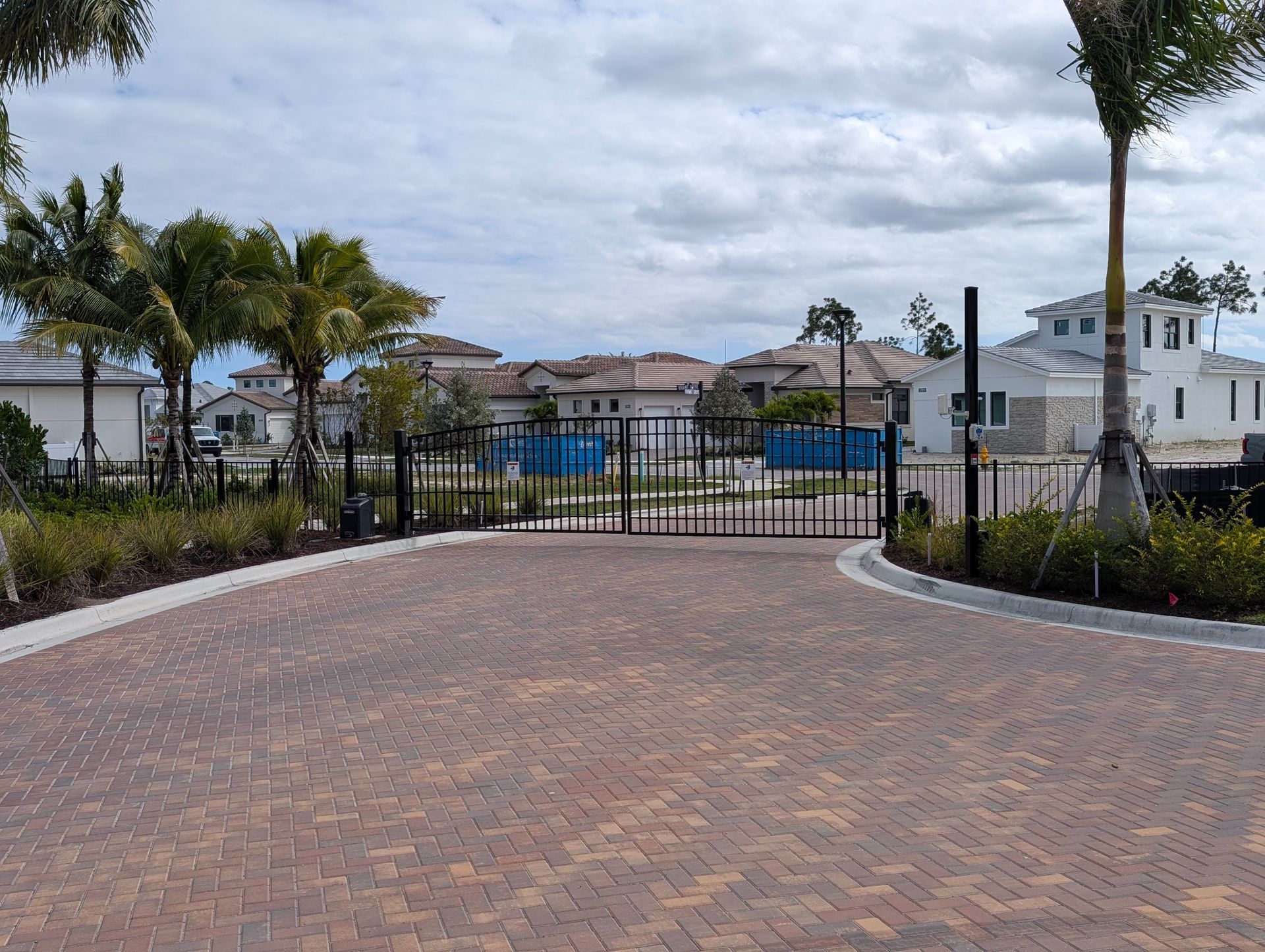 Gated waterfront driveway with palm trees and brick paving leading to homes and a canal