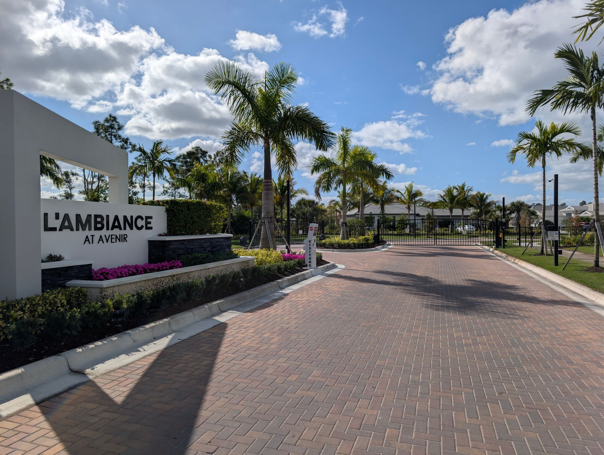L’AMBiANCE at Vivé sign beside a palm-lined brick road under a partly cloudy sky