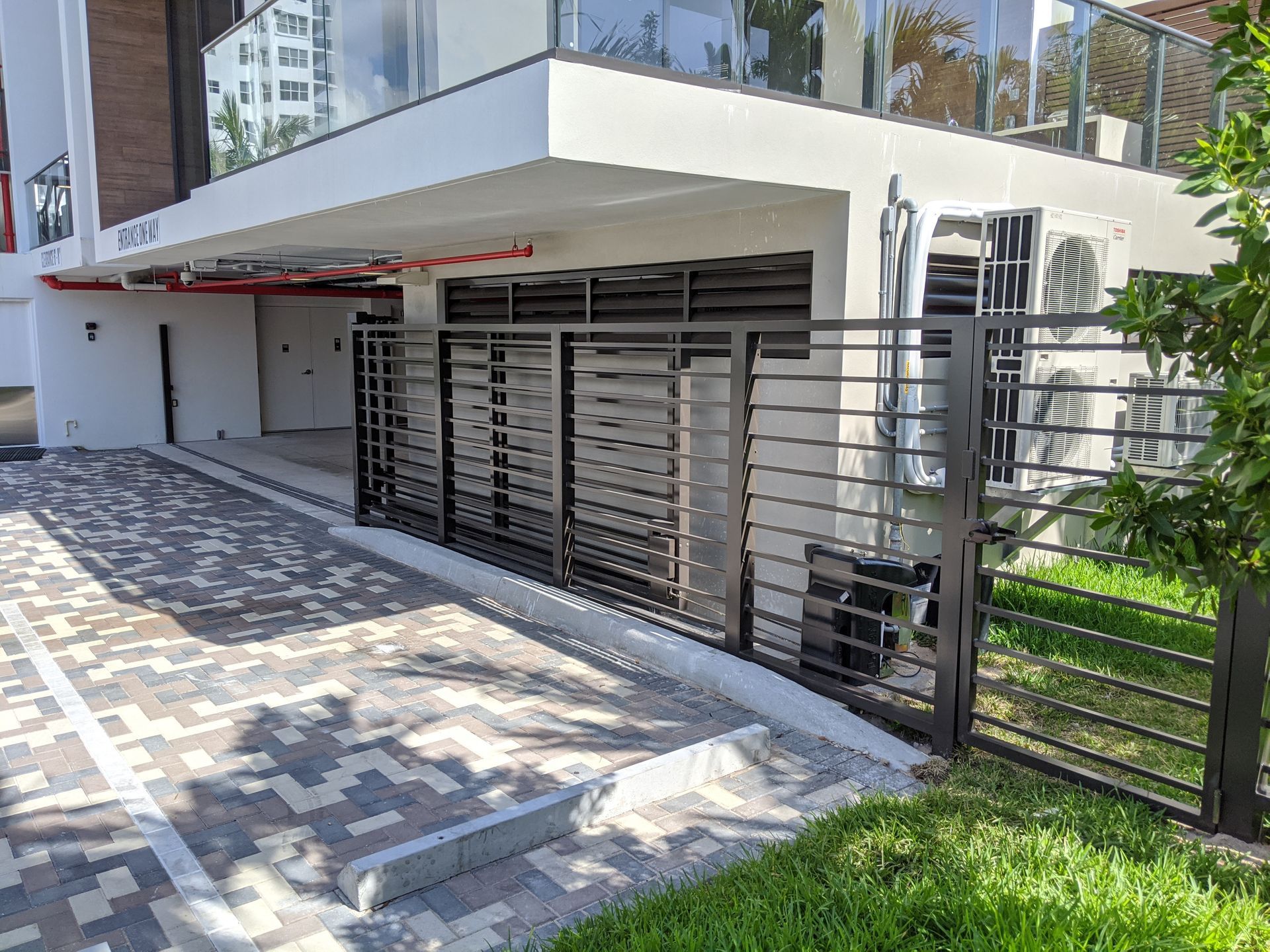 Modern building entrance with metal gate, paved walkway, and landscaped greenery