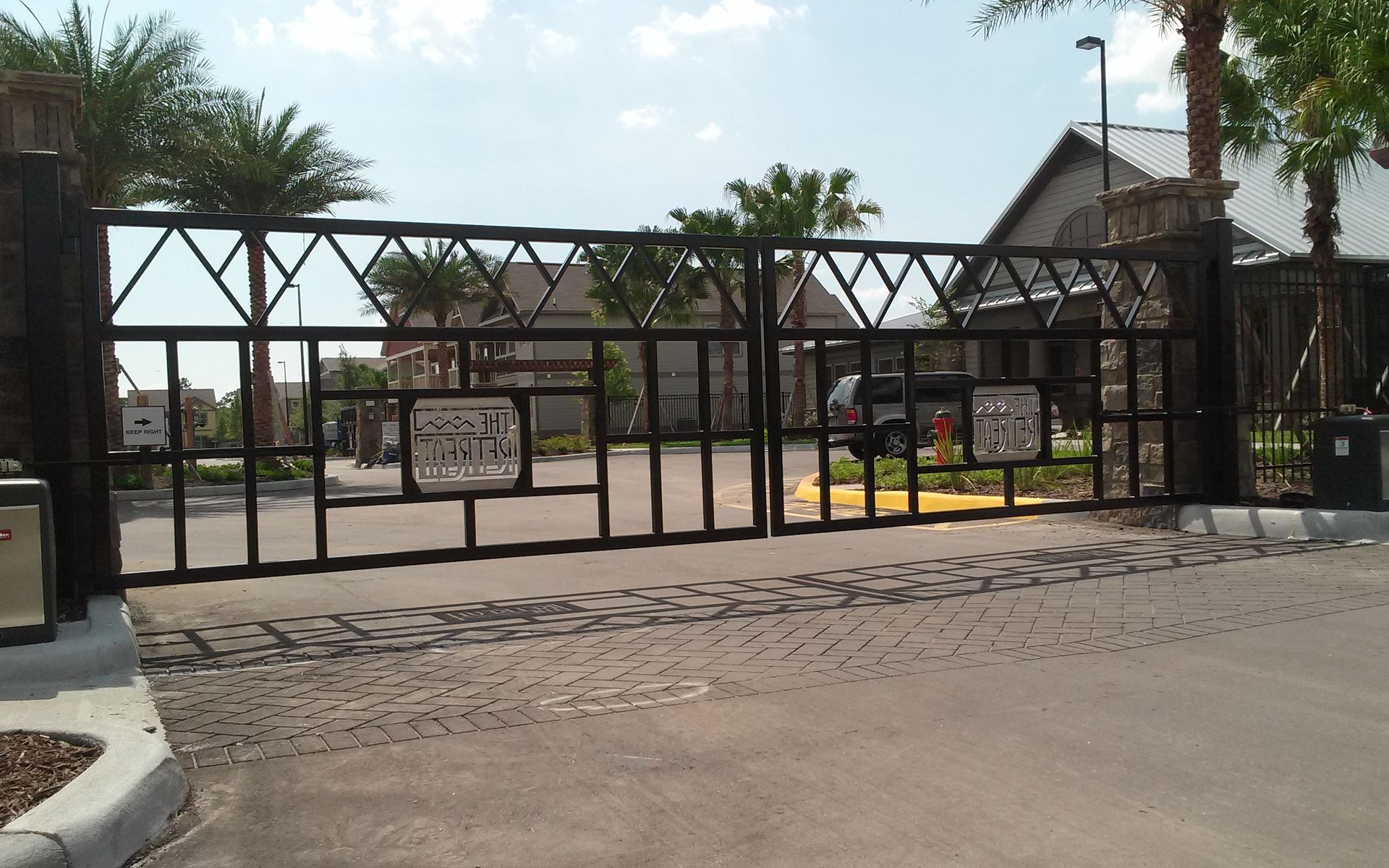 Gated entrance with black metal fence and sliding gate in front of a building on a sunny day