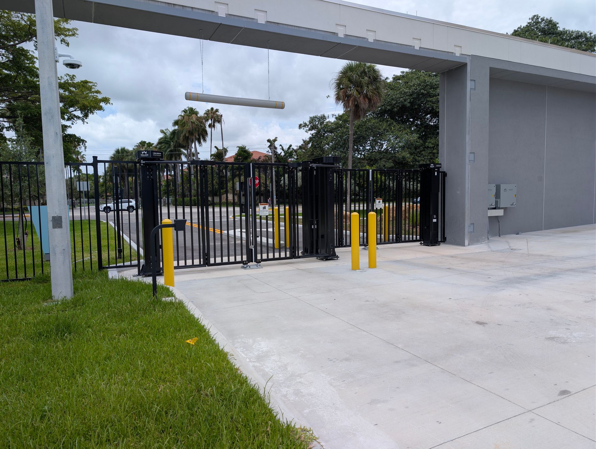 Black metal gate at a driveway entrance beside a grassy lawn and concrete building