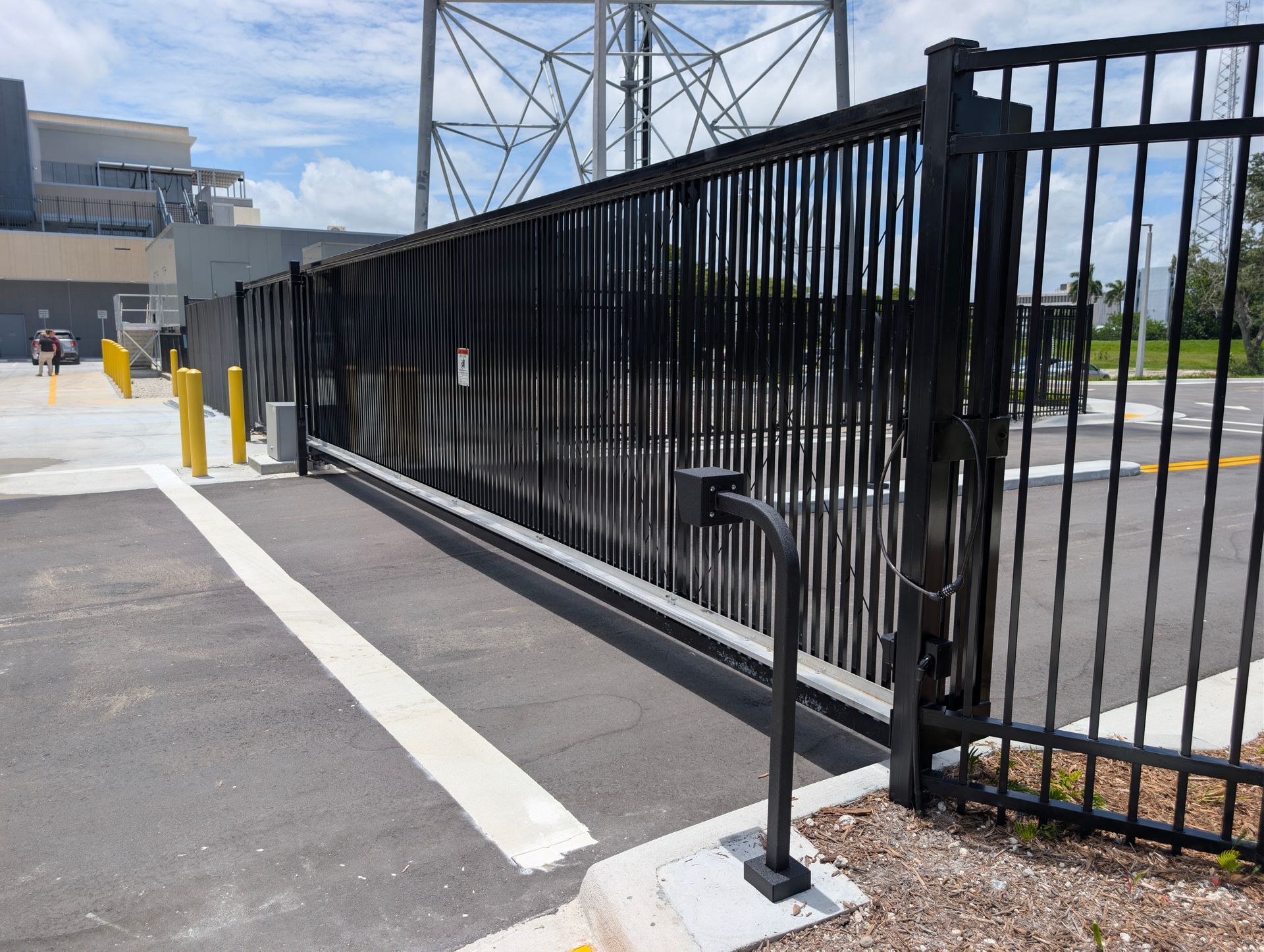 Black metal security fence beside a paved driveway and sidewalk outside a modern building