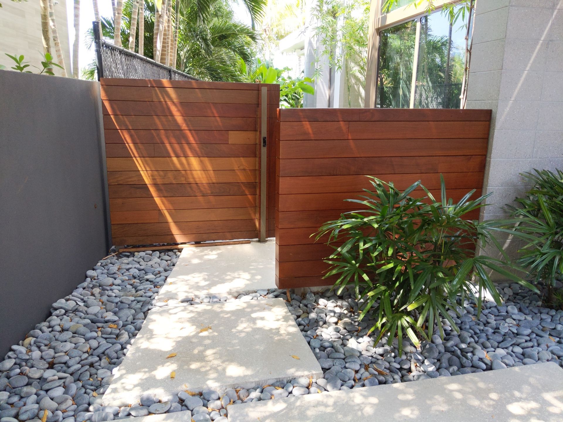 Modern front yard with a concrete path, gray rocks, wooden fence panels, and green shrubs