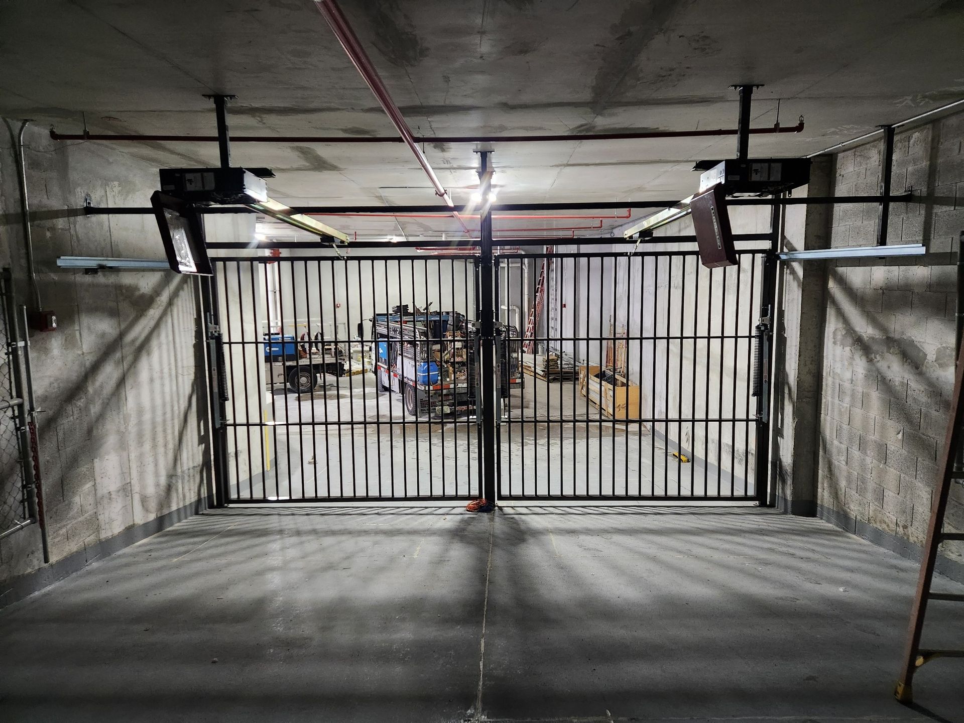 Gated underground utility room with concrete walls, pipes, and equipment behind a metal barrier