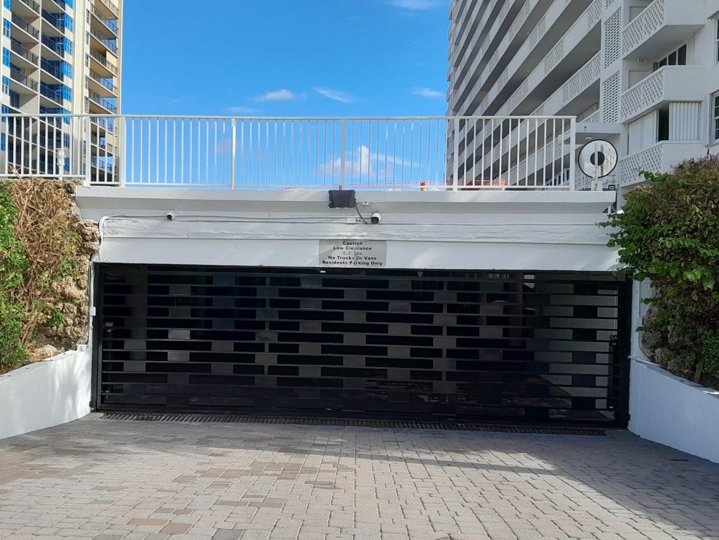 Modern apartment garage entrance with a black gate between white buildings and a tiled driveway