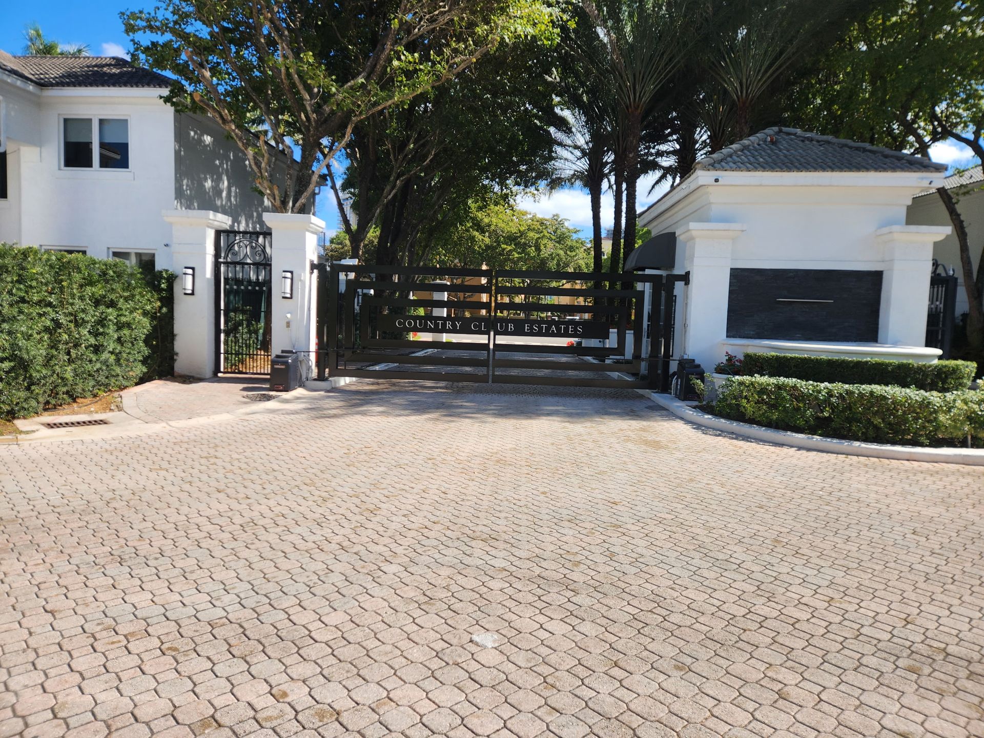 Gated driveway to a white house with trees and a garage on the right
