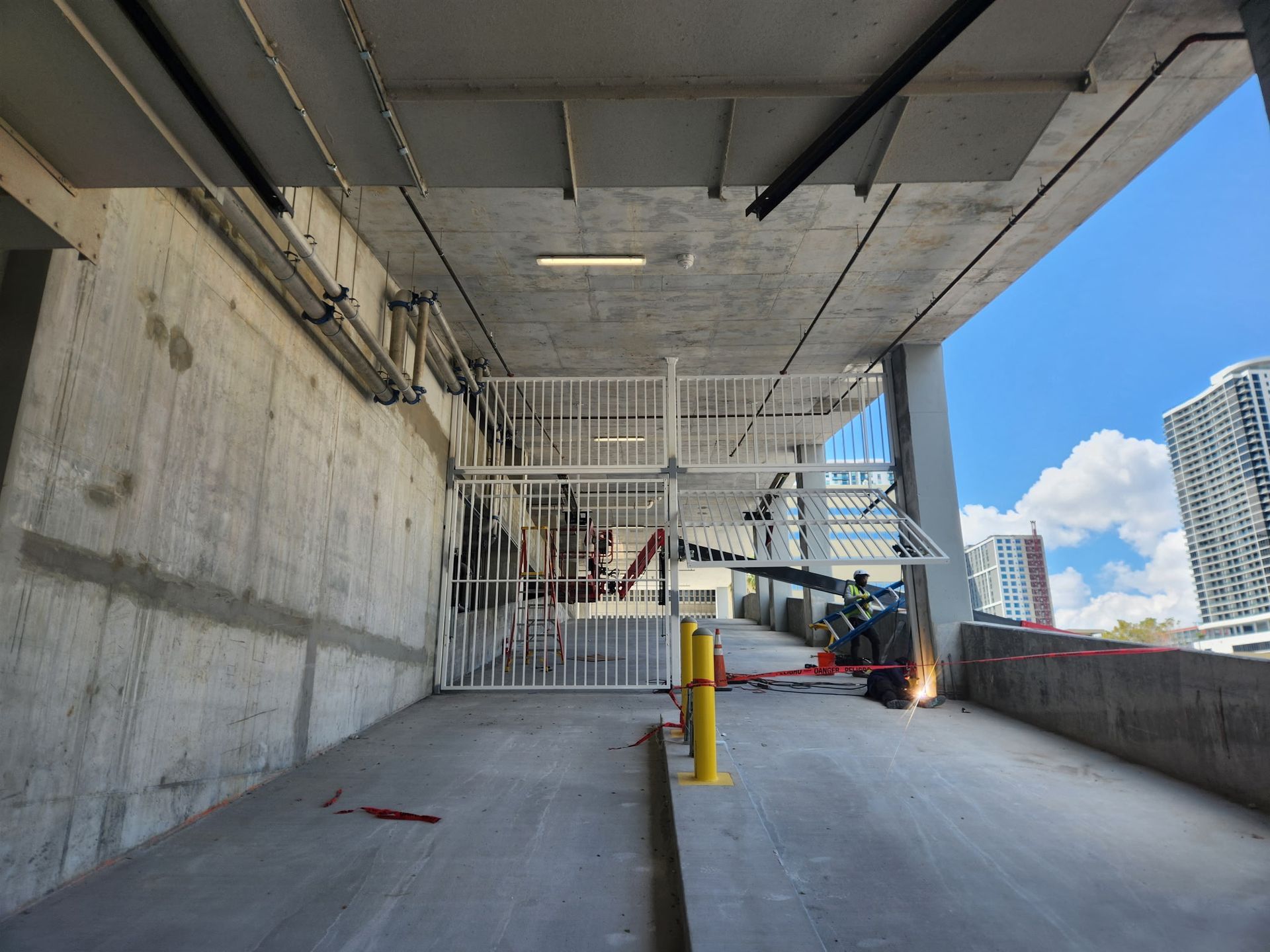 Covered parking ramp with concrete walls, yellow bollard, and a person working near sparks at the far end