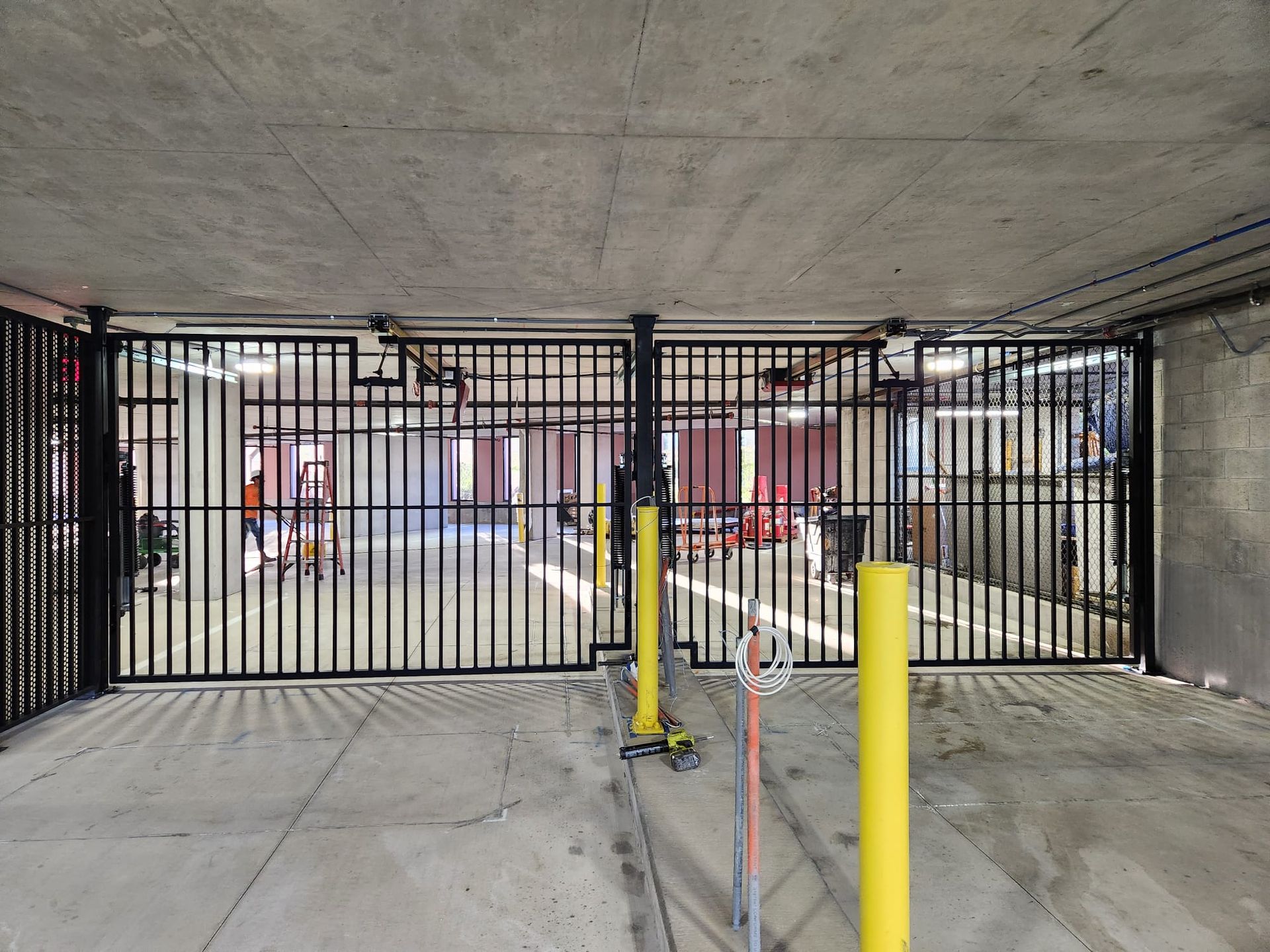 Closed black metal gate in a concrete parking garage entrance with yellow bollards and a pedestrian door.