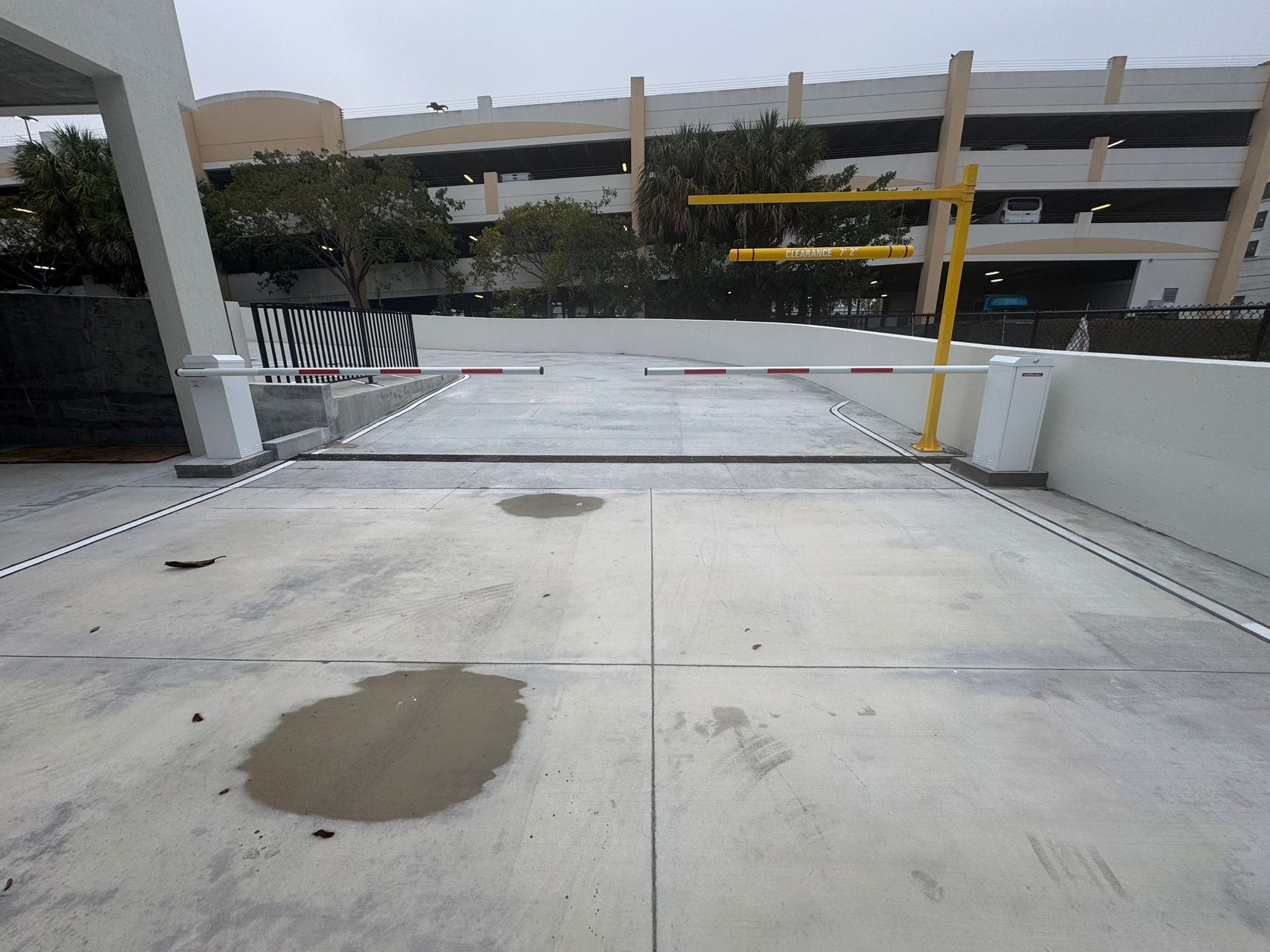 Parking garage entrance with a yellow gate arm and concrete roadway with wet patches.
