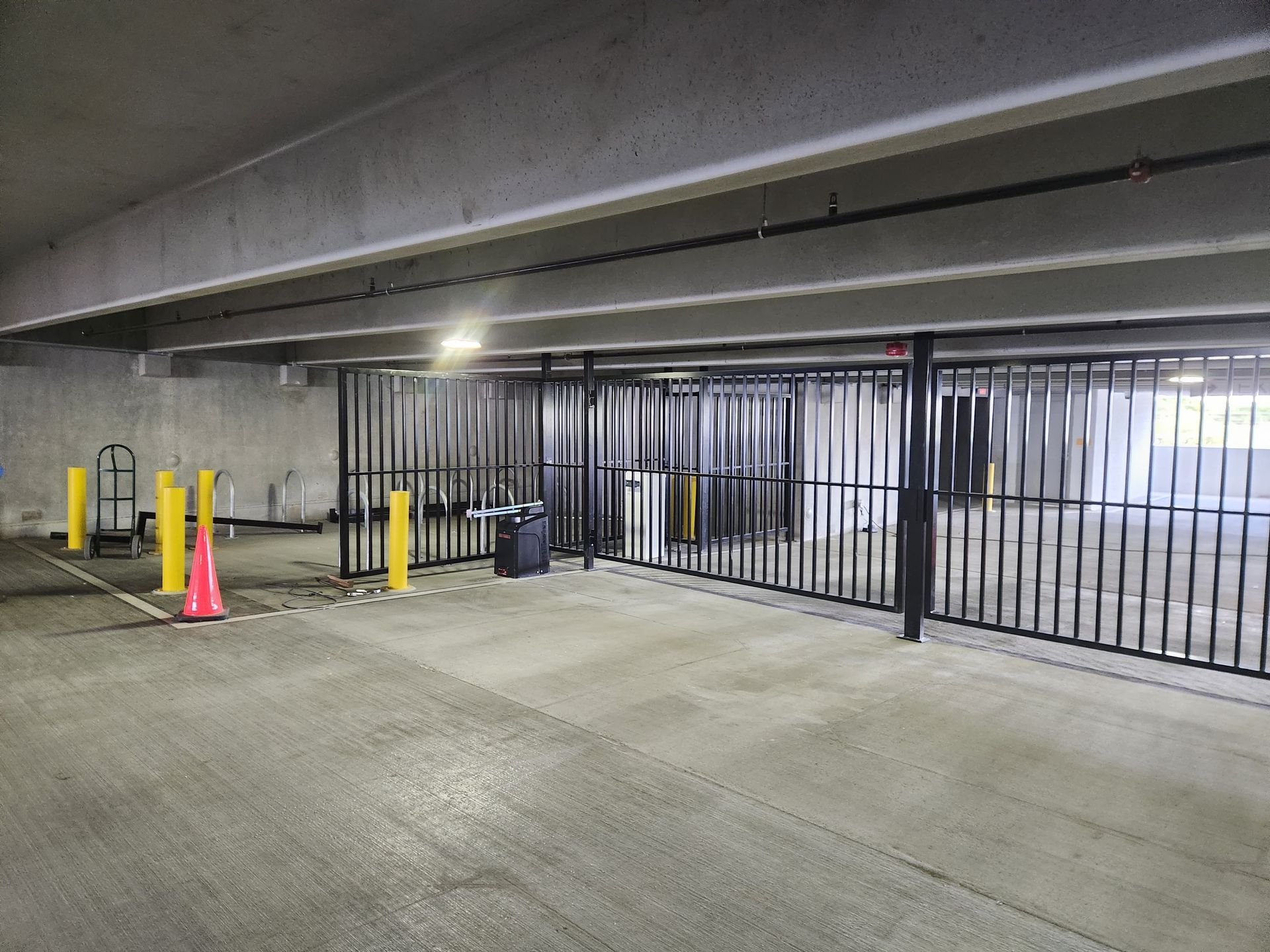 Empty parking garage entry with metal gate, yellow bollards, and a pink cone.