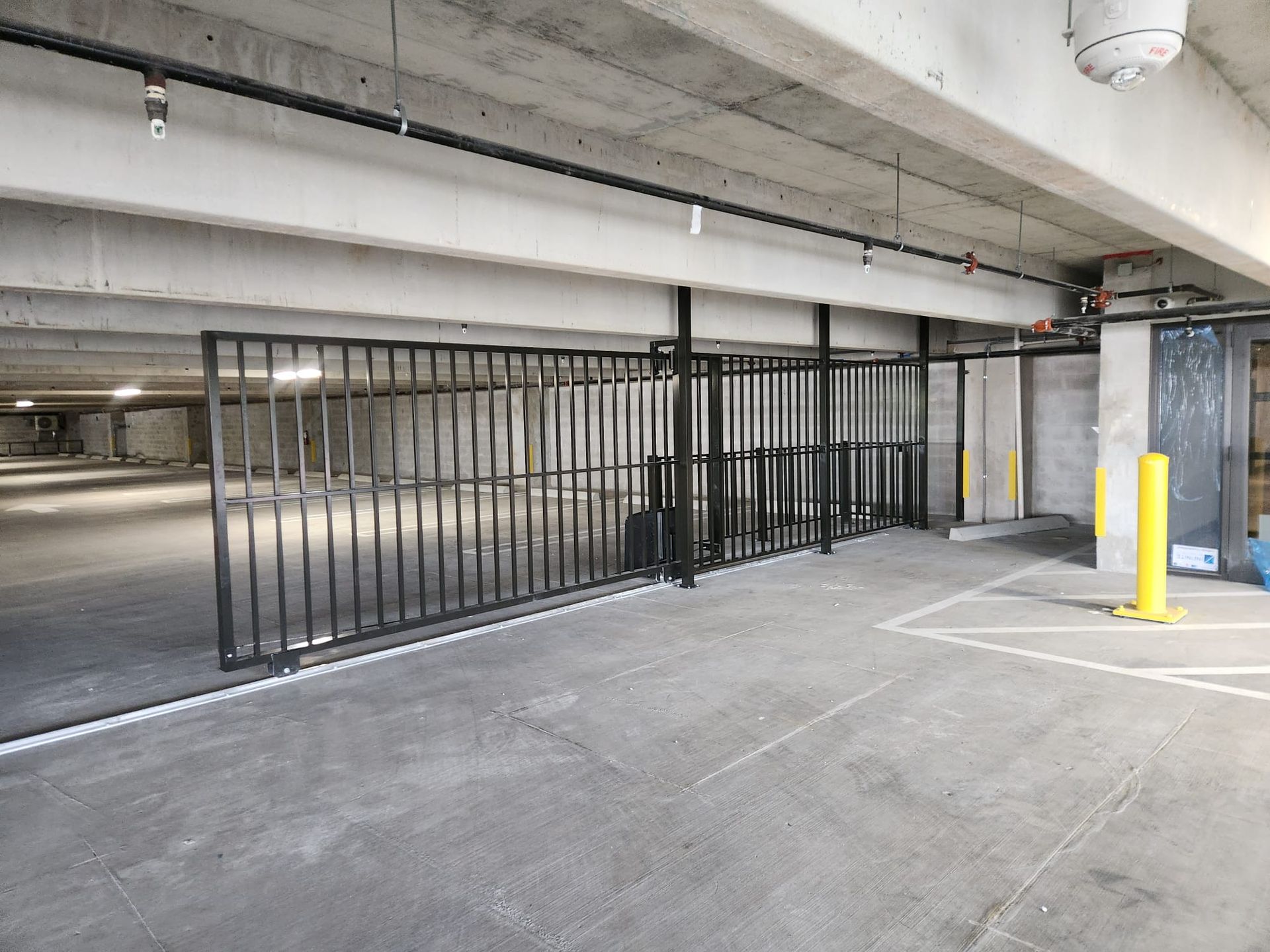 Parking garage entrance blocked by a black metal gate with yellow bollards nearby