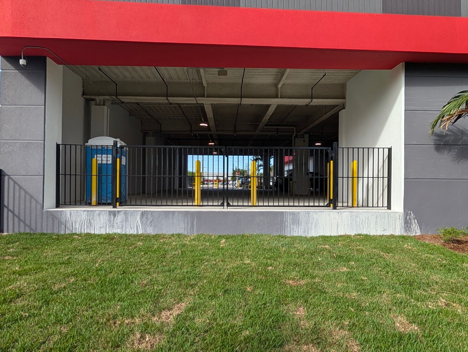 Covered entrance with red awning, black railing, and yellow bollards above a grassy slope