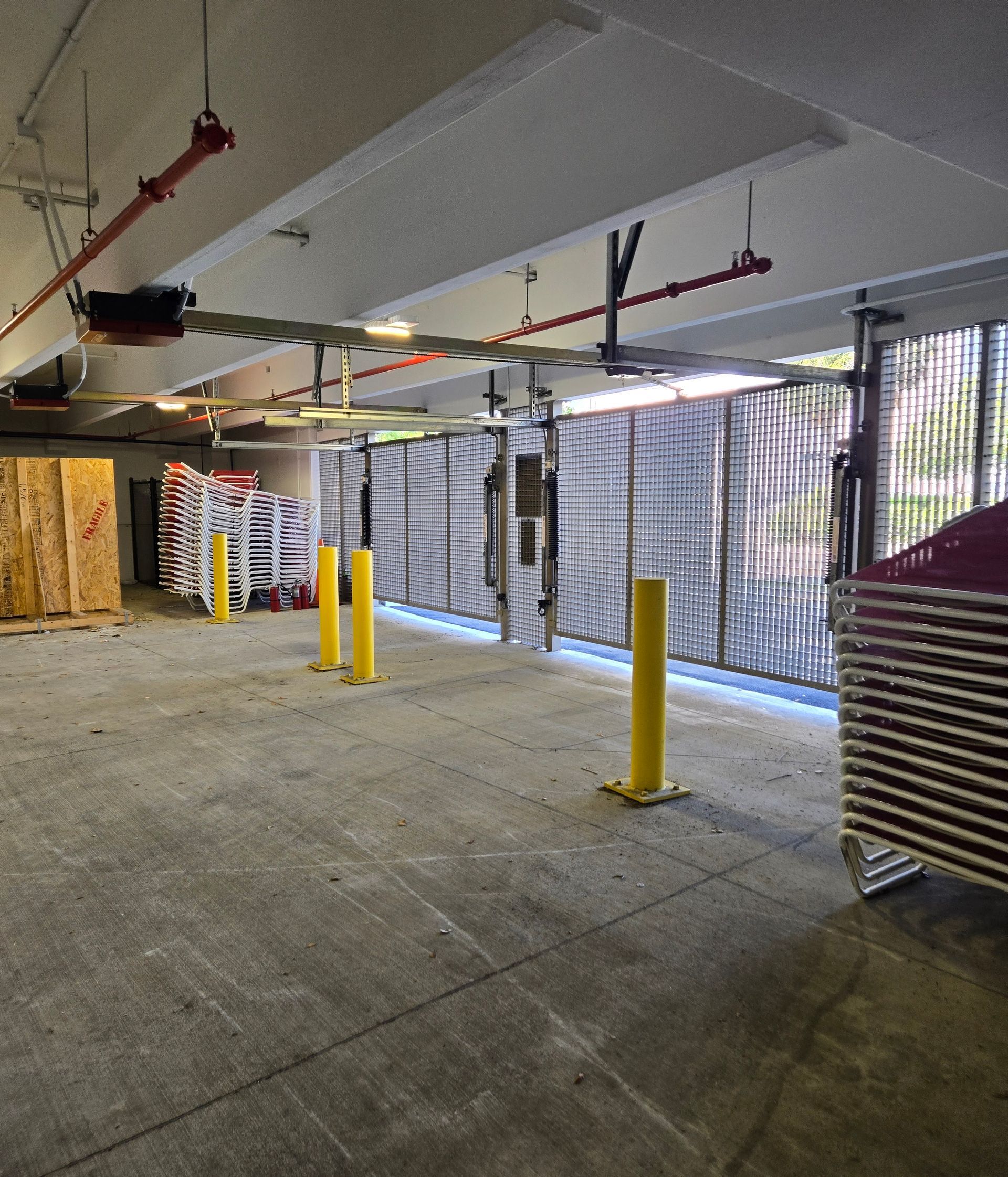Empty indoor parking garage with yellow bollards and overhead pipes, lit by fluorescent lights.