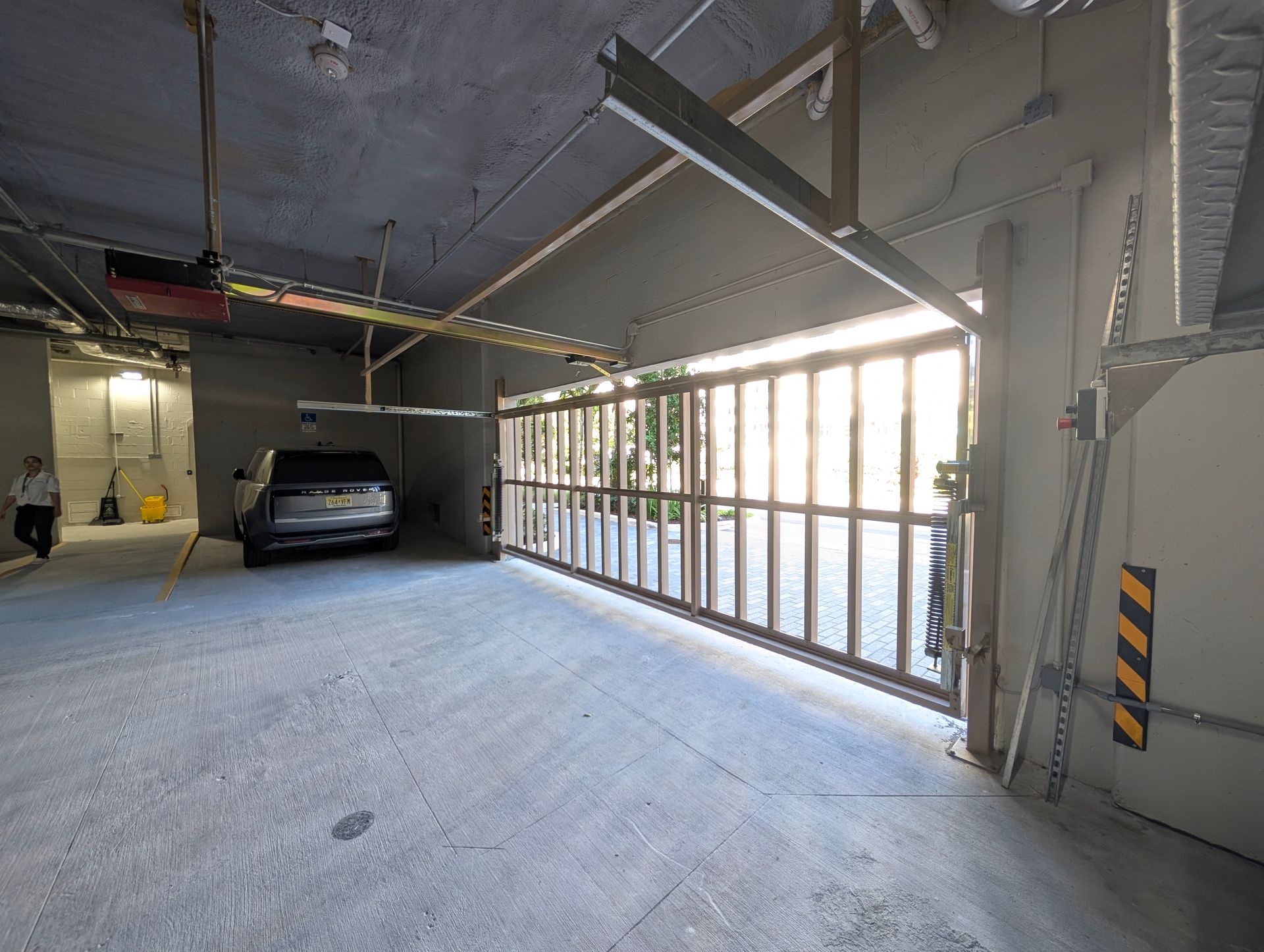 Covered parking garage with a car on the left and bright daylight through a glass wall on the right