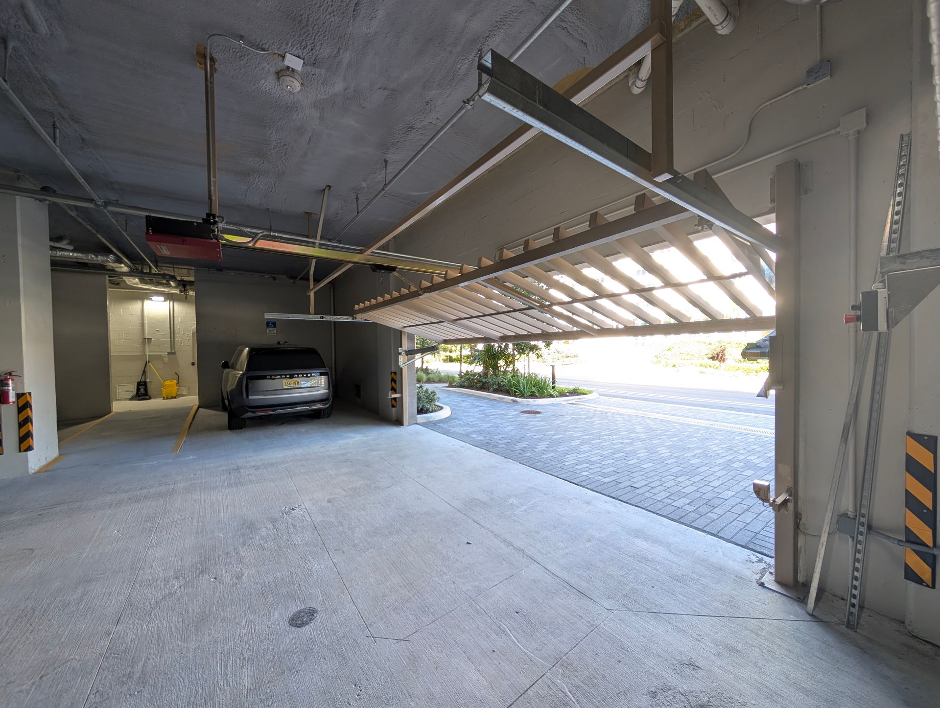 Covered parking garage with a raised driveway gate, parked car, and bright outdoor light beyond.