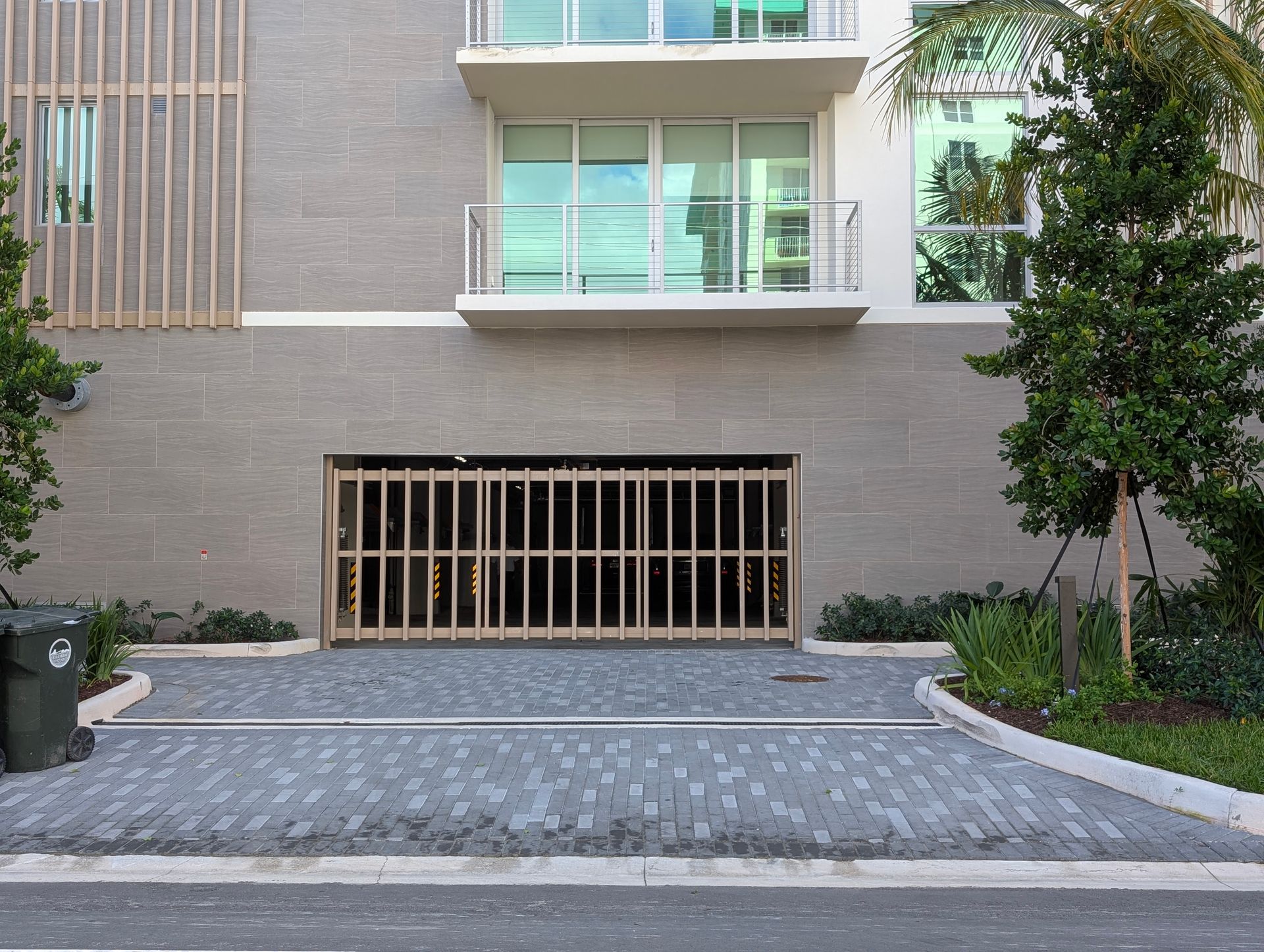 Modern apartment building facade with a gated garage entrance and landscaped driveway