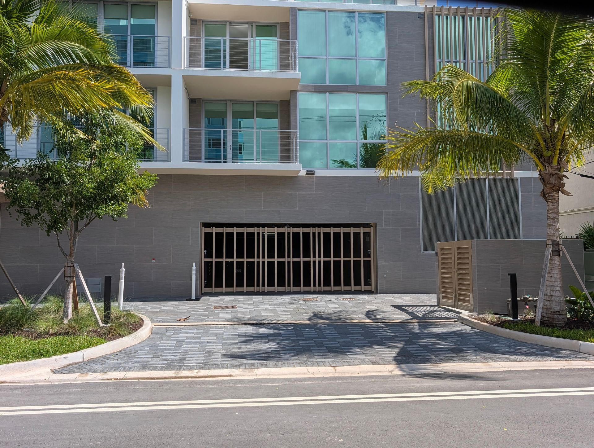 Modern apartment building entrance with balconies, palm trees, and a closed garage gate
