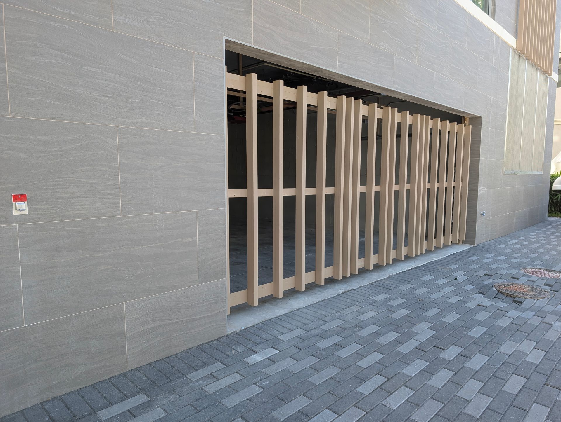 Modern building exterior with a large metal-barred opening and gray tiled walkway