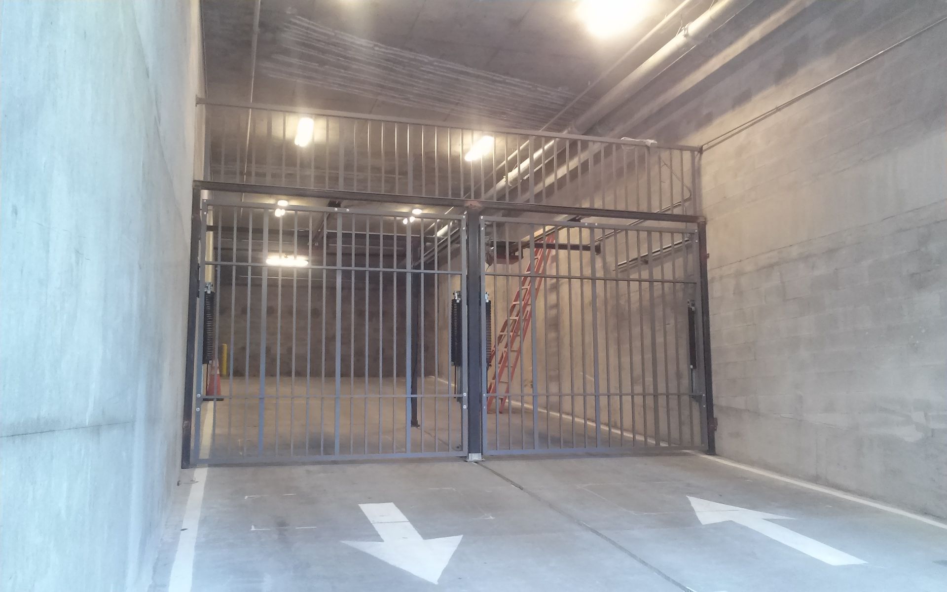 Indoor gated parking area with concrete floor, overhead lights, and white directional arrows.