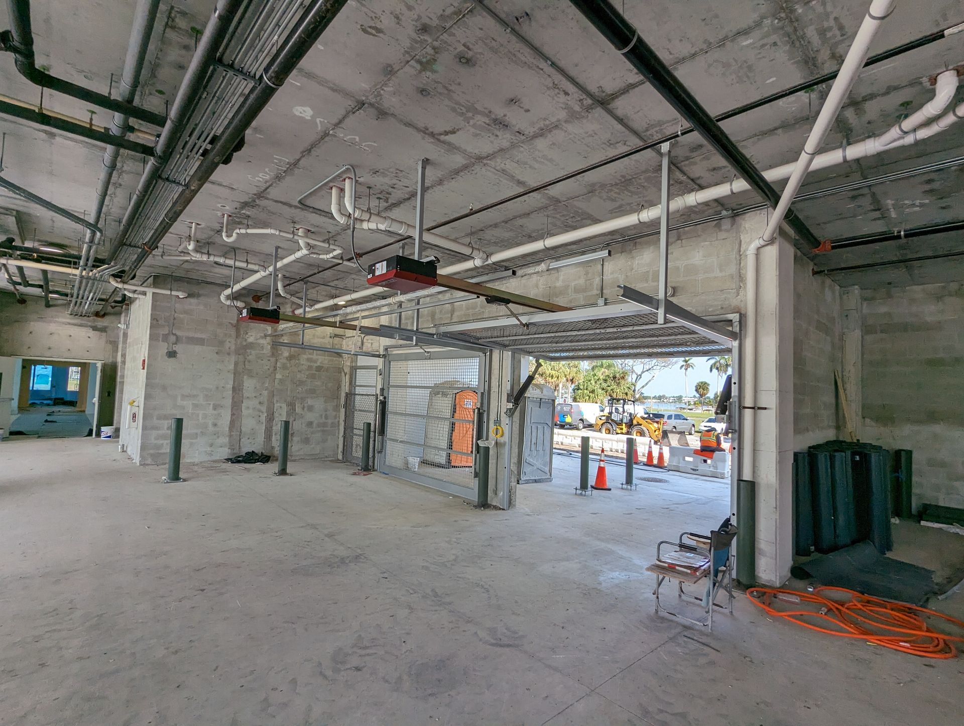 Unfinished commercial interior with exposed ceiling, concrete floor, and construction materials near an open doorway.