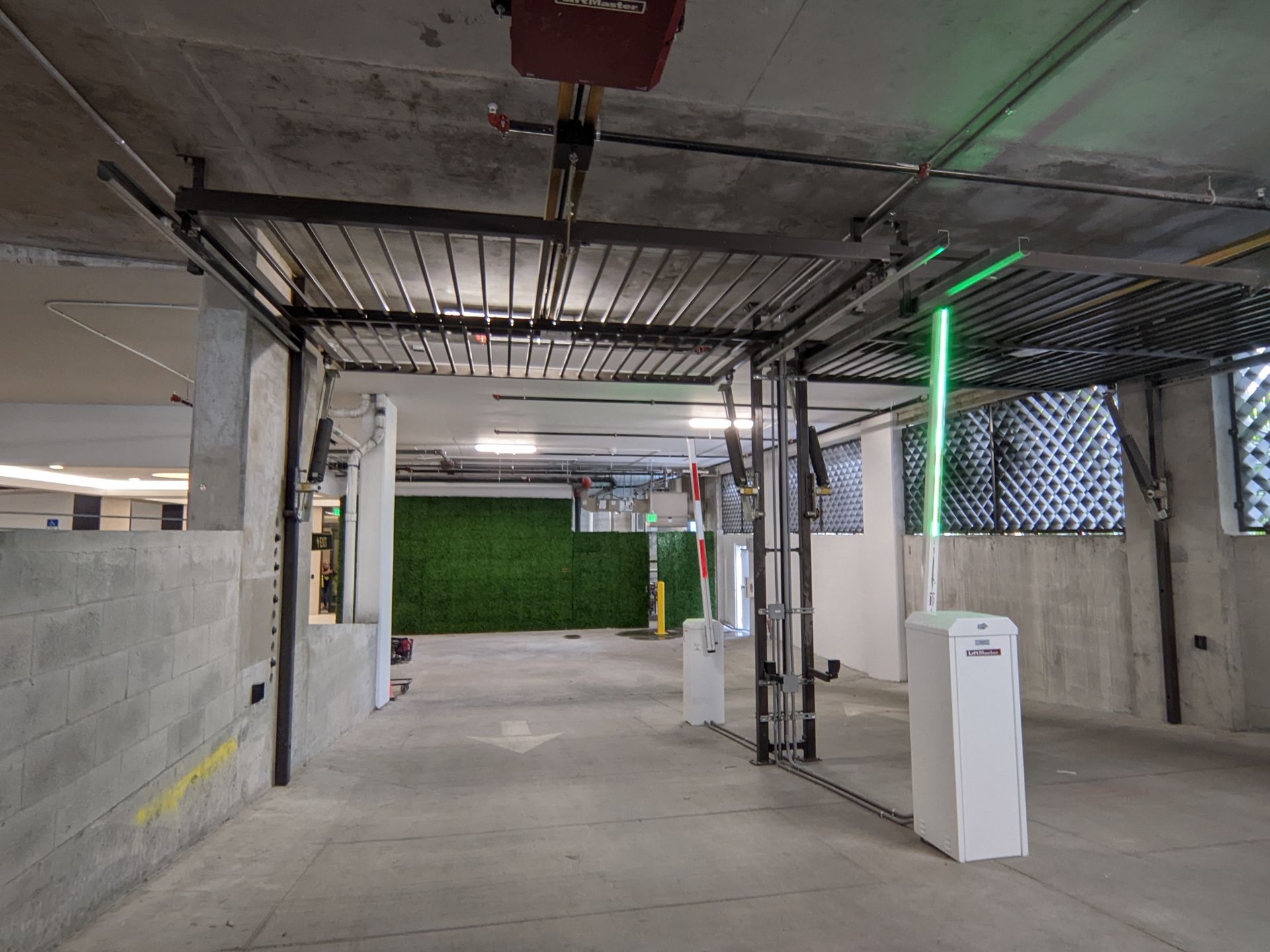 Covered parking area with concrete walls, green accent lighting, and a gated entrance in the distance