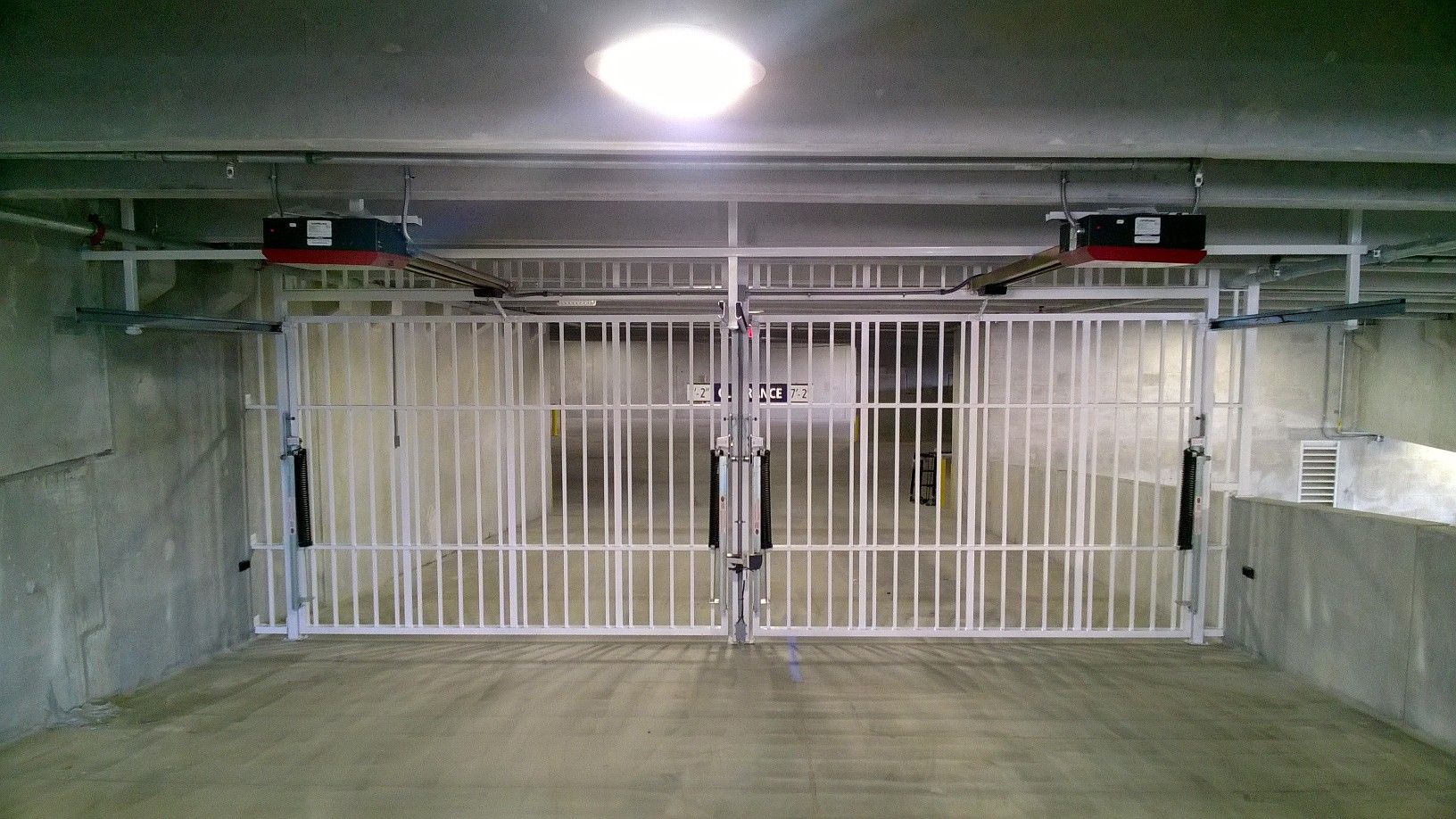 Concrete parking garage with closed white metal security gates under fluorescent lights
