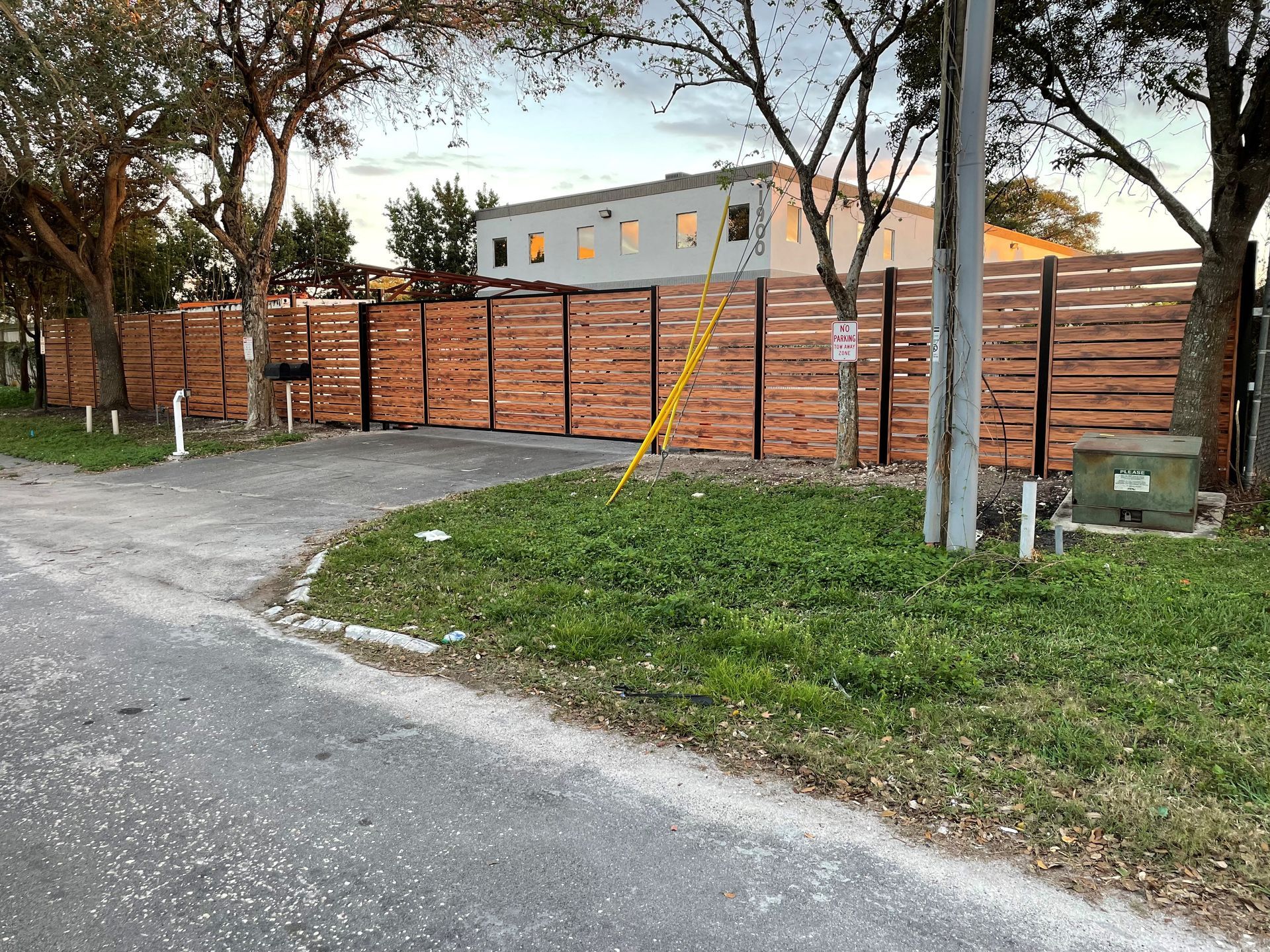 Brick wall and metal gate beside a gravel road, with a grassy verge and trees at dusk.