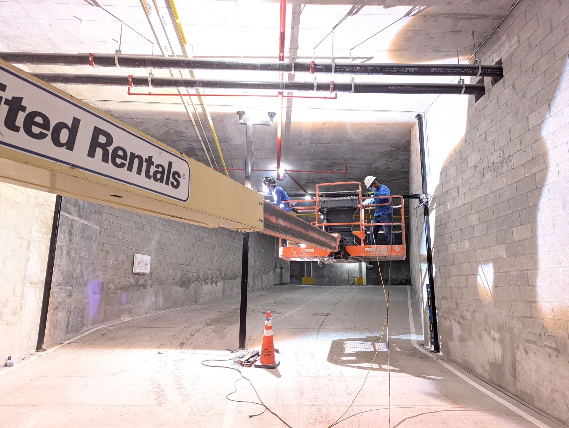 Construction lift inside unfinished concrete room with workers in orange safety gear.