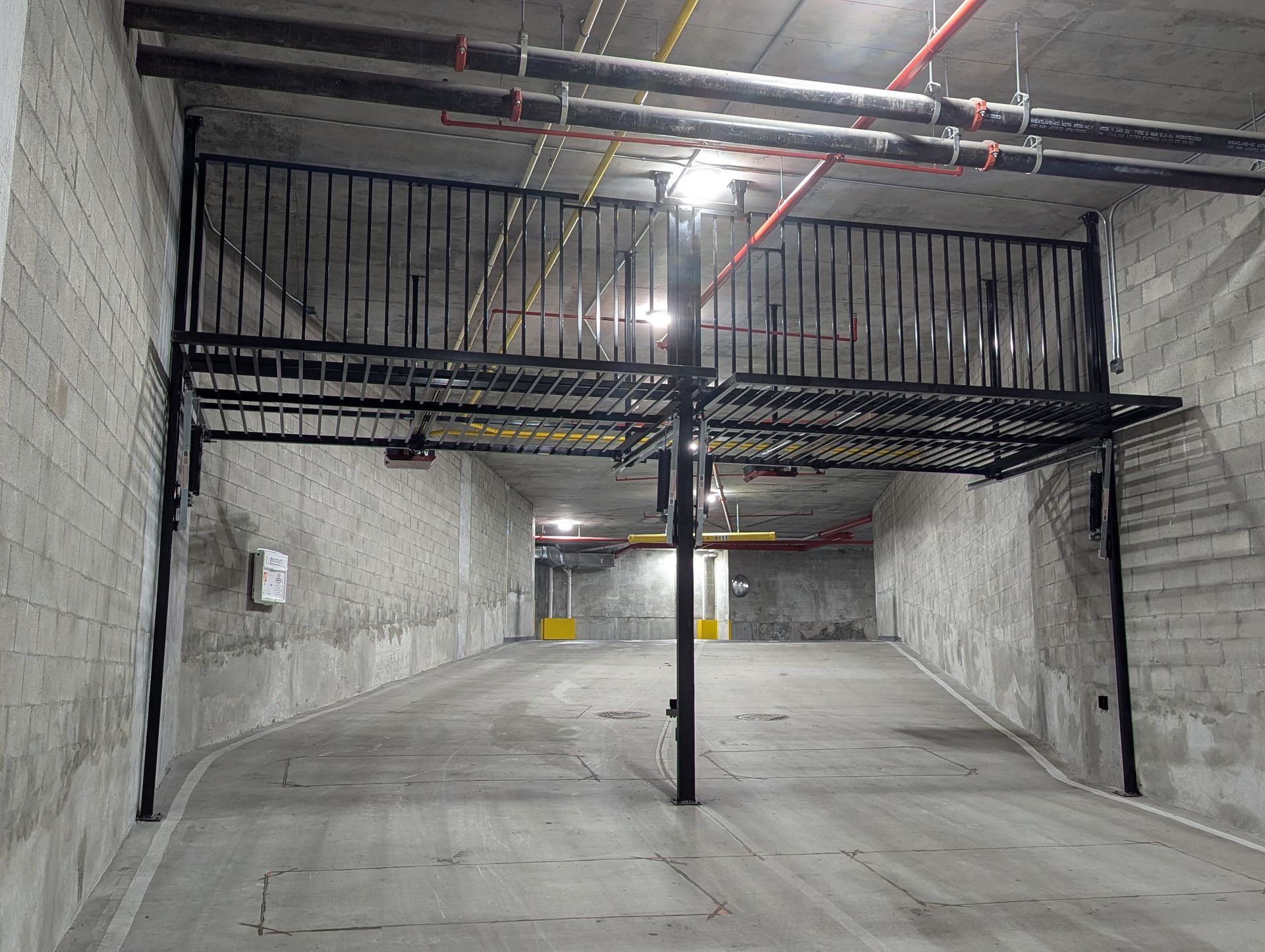 Empty concrete parking garage with a low black metal mezzanine and overhead pipes