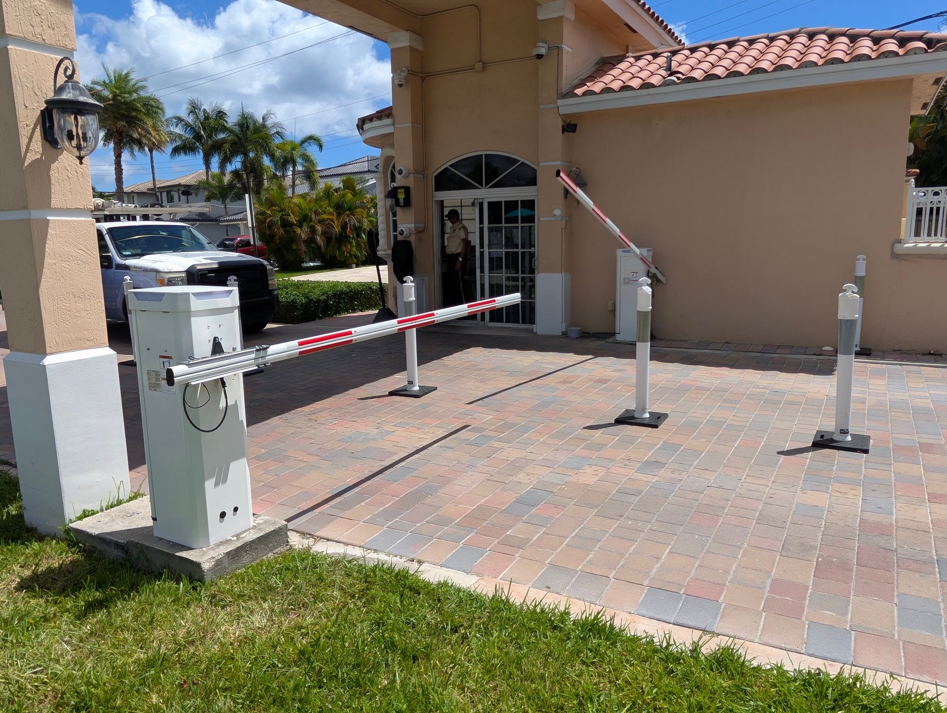 Parking lot entry with red-and-white barrier arm, payment kiosk, and bollards beside a stucco building under blue sky