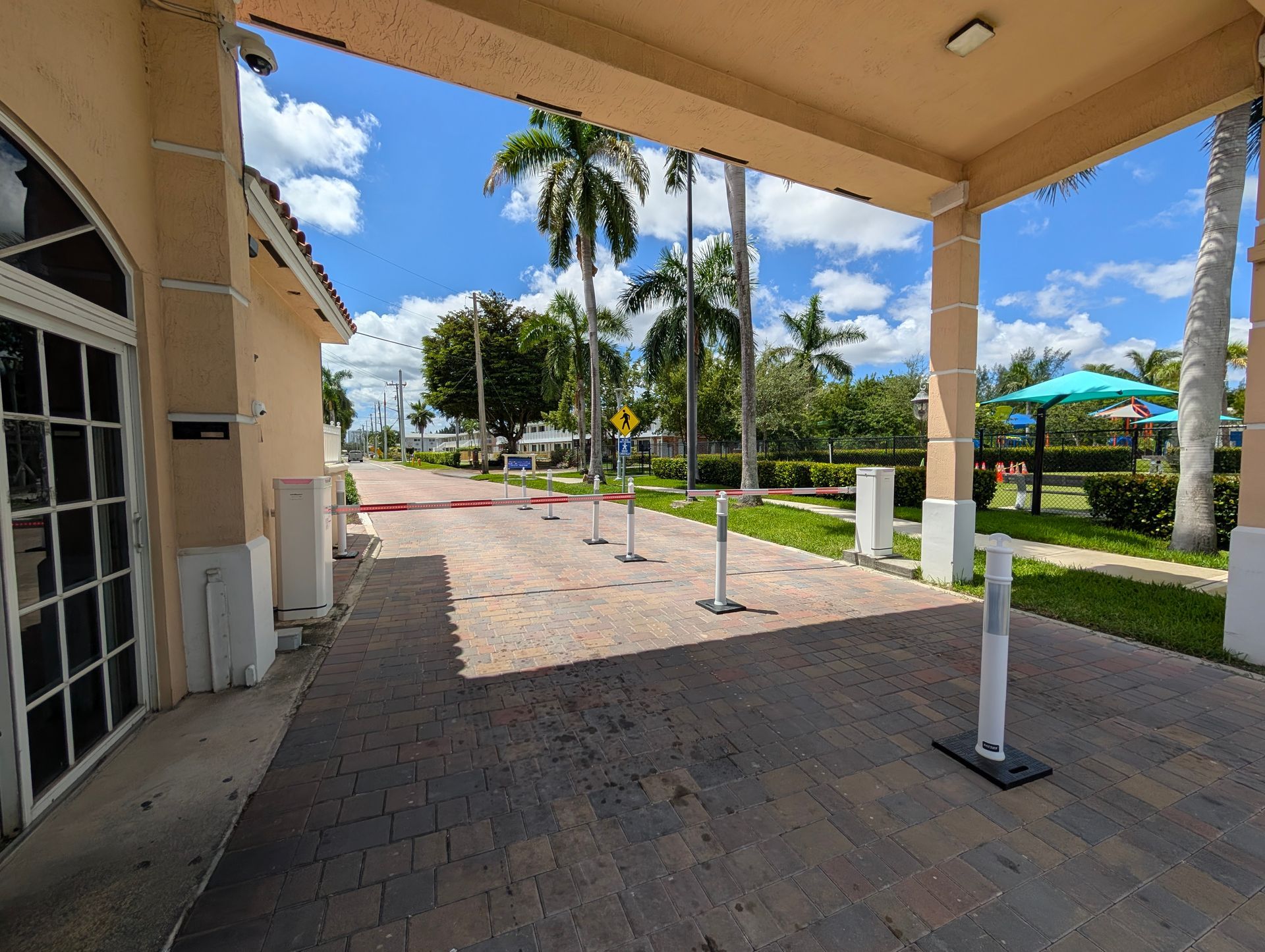 Covered walkway beside a tropical resort path with palm trees, white columns, and blue sky