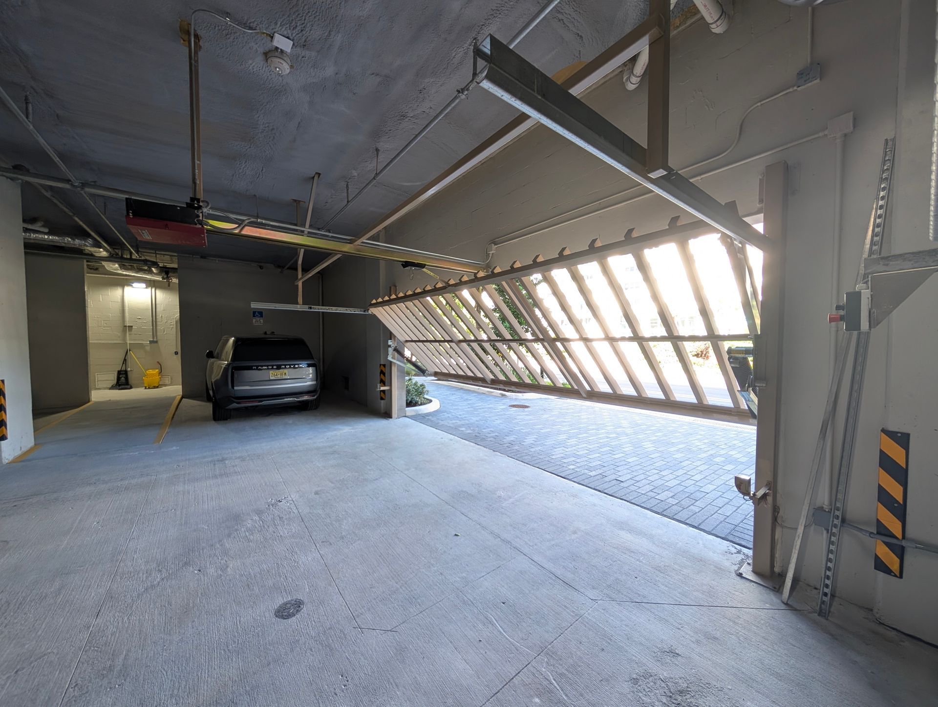 Underground parking garage with a car and a partially raised metal gate letting in sunlight