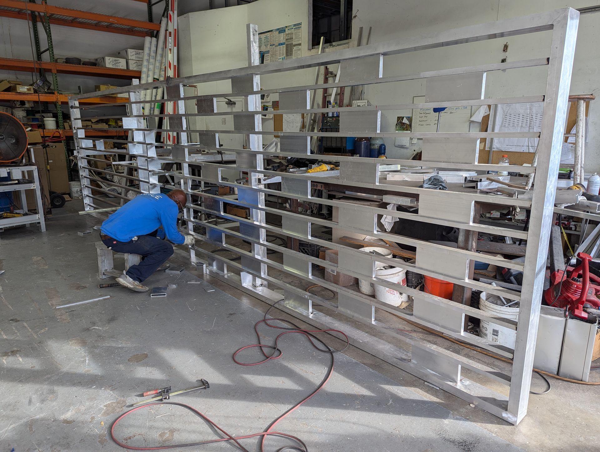 Worker assembling a large white metal gate in a warehouse workshop