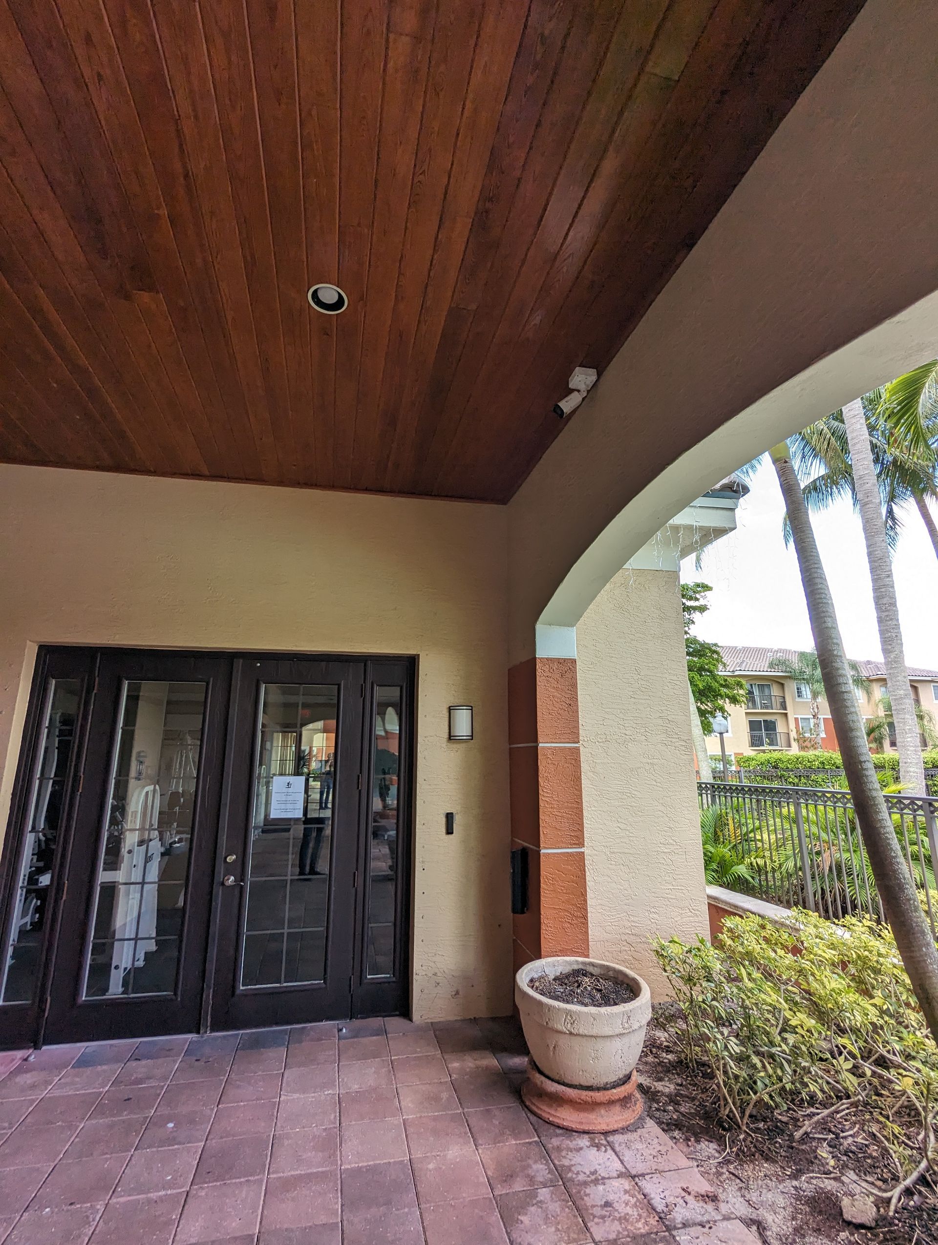 Covered front entry with dark double doors, wood ceiling, and potted planter beside an archway.
