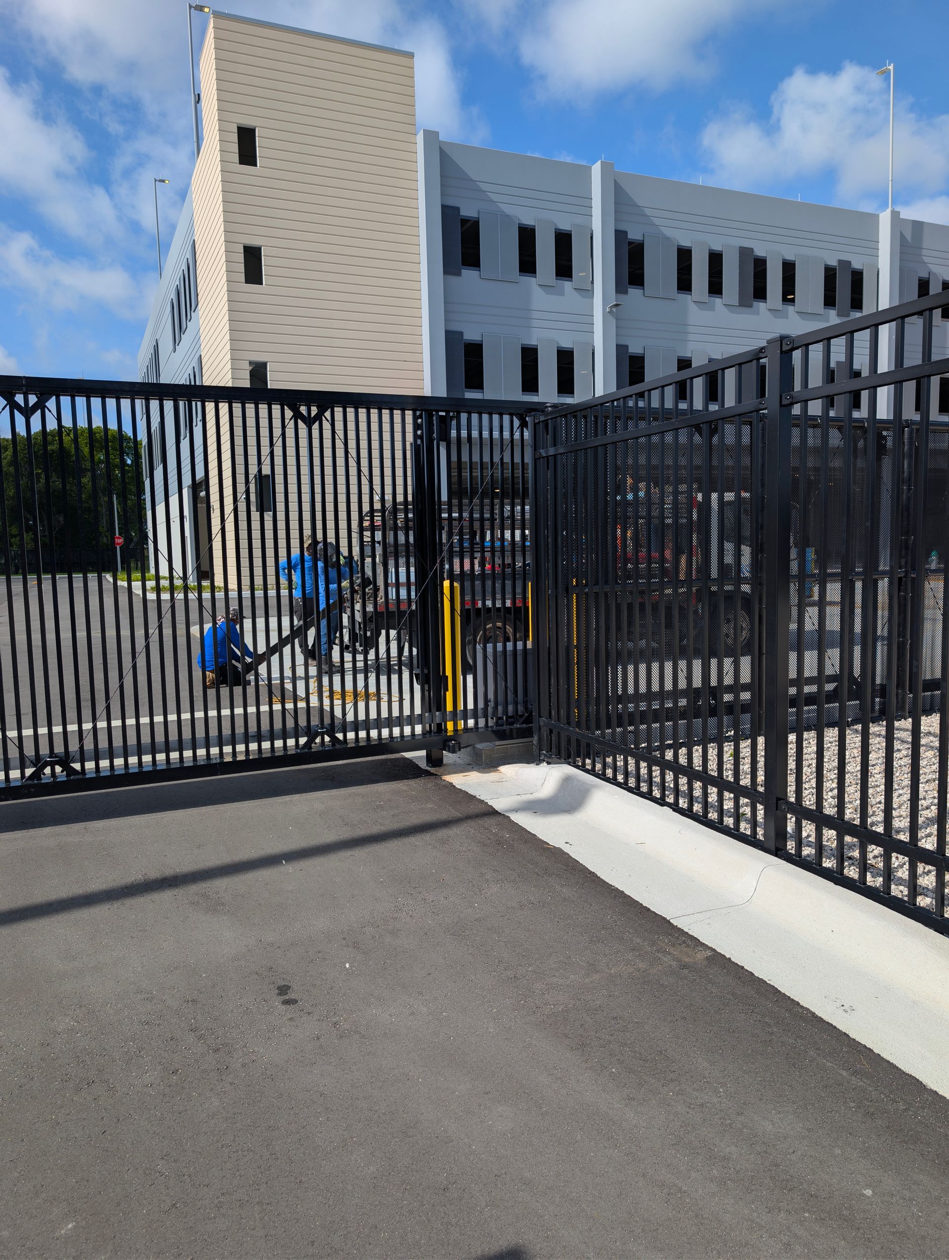 Black metal gate beside a white building, with a blue bicycle parked inside the fenced area.